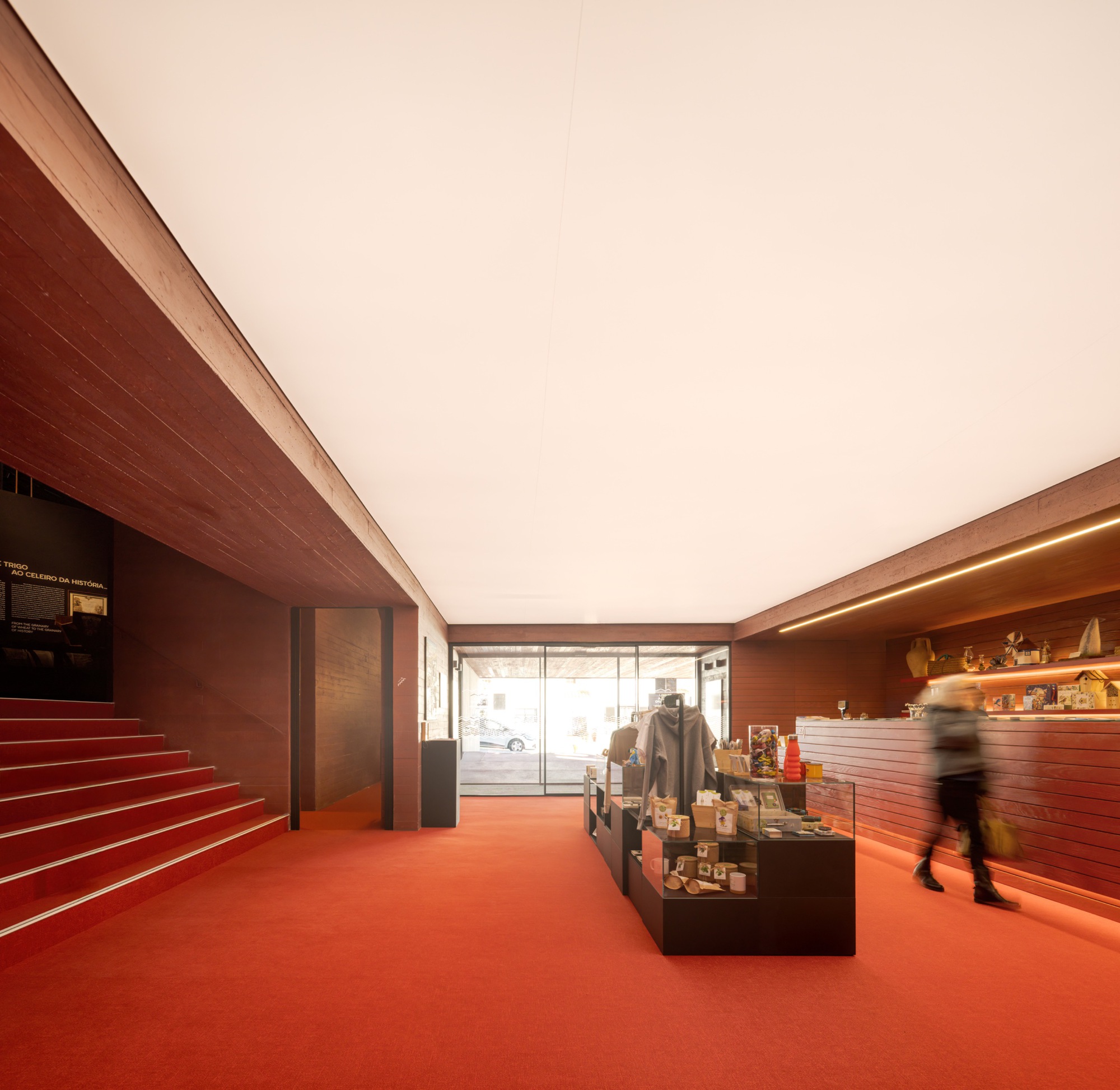 Museum shop interior with red resin floor, wood-clad walls and a visitor in motion