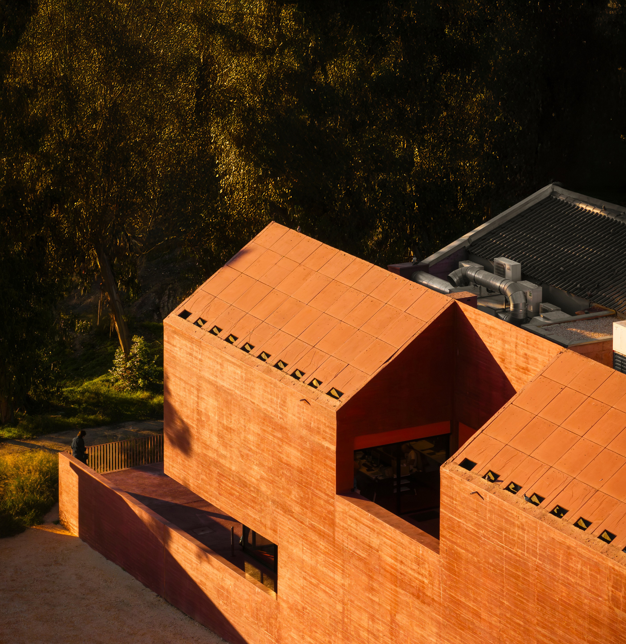 Aerial view of the orange tiled roof volumes with deep angular cutouts at golden hour
