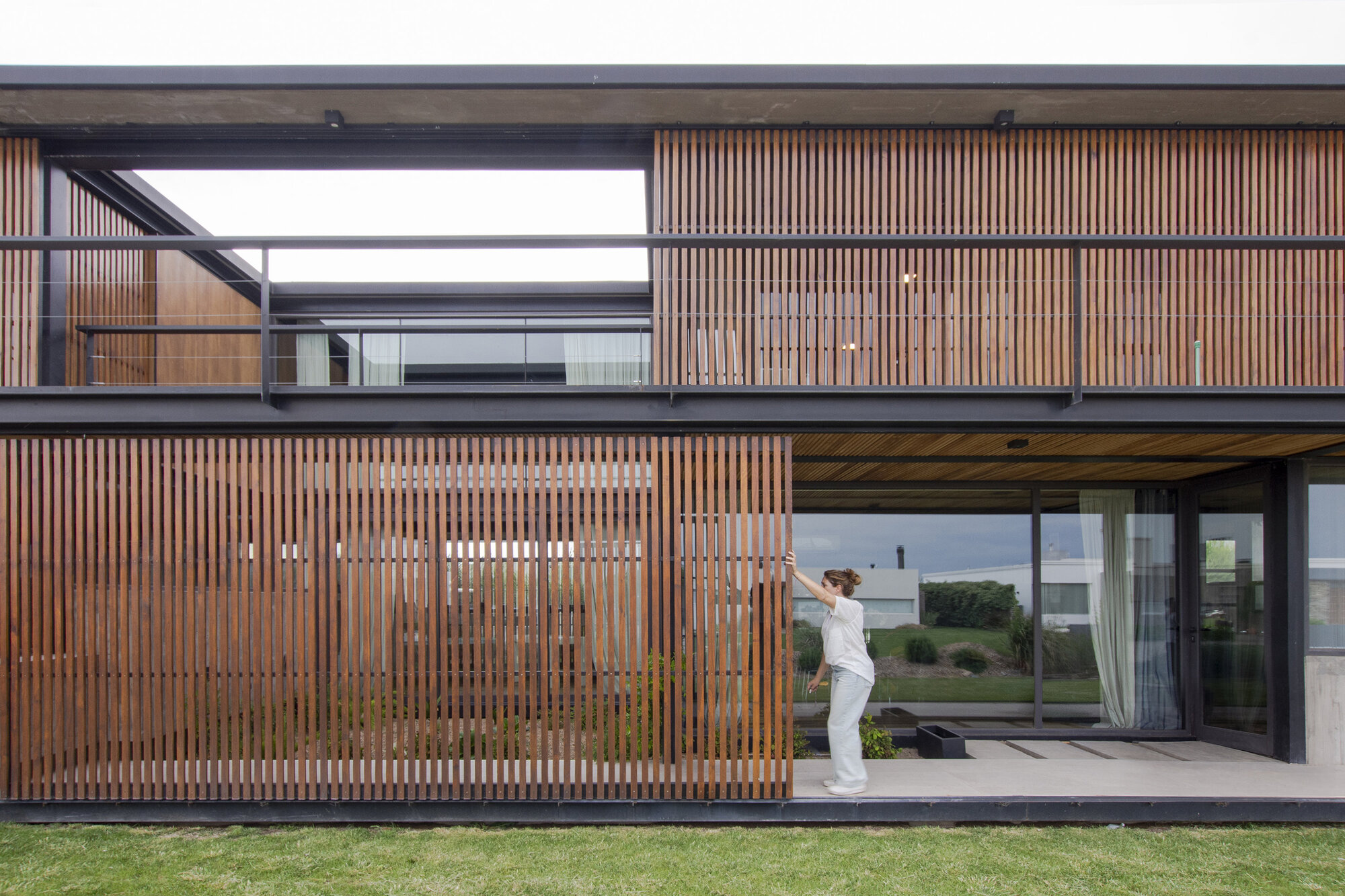 Vertical timber screen facade with sliding panels and glass doors where a figure stands on the terrace