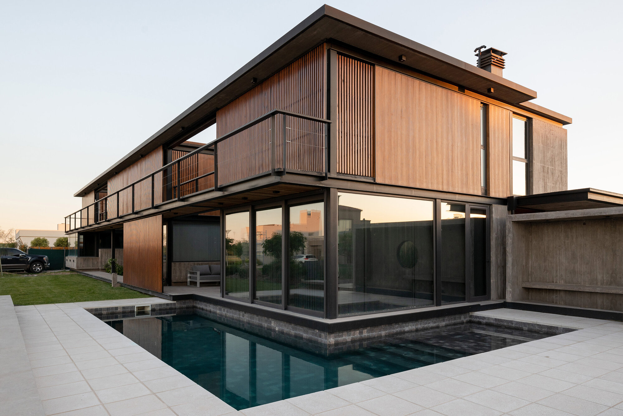 Two-level residence with timber cladding and vertical slat screens overlooking a pool at dusk