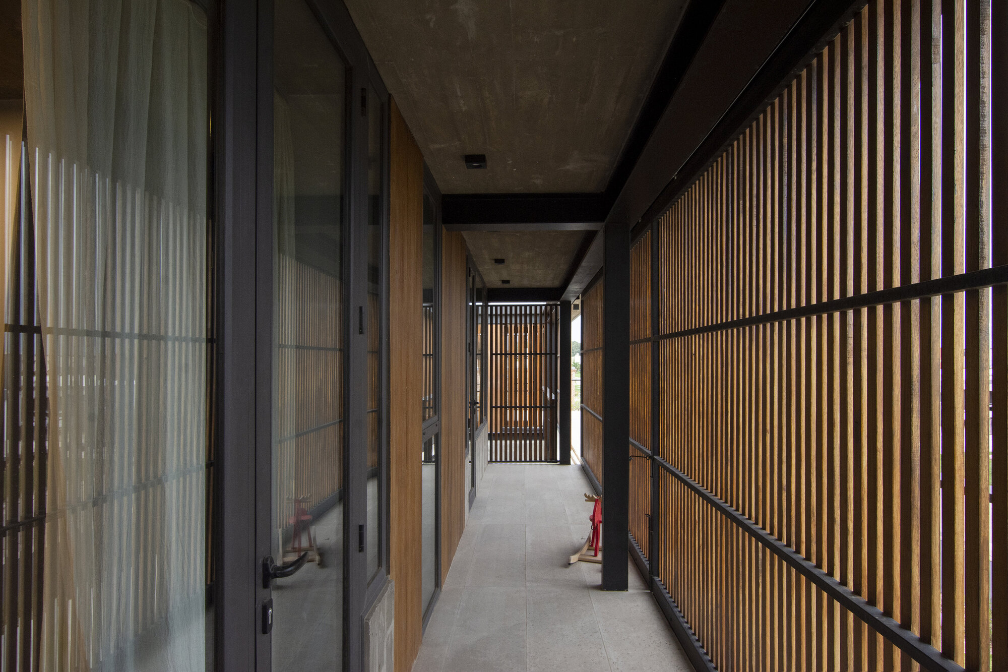 Corridor with concrete ceiling beams and vertical timber screens on one side with glazing on the other