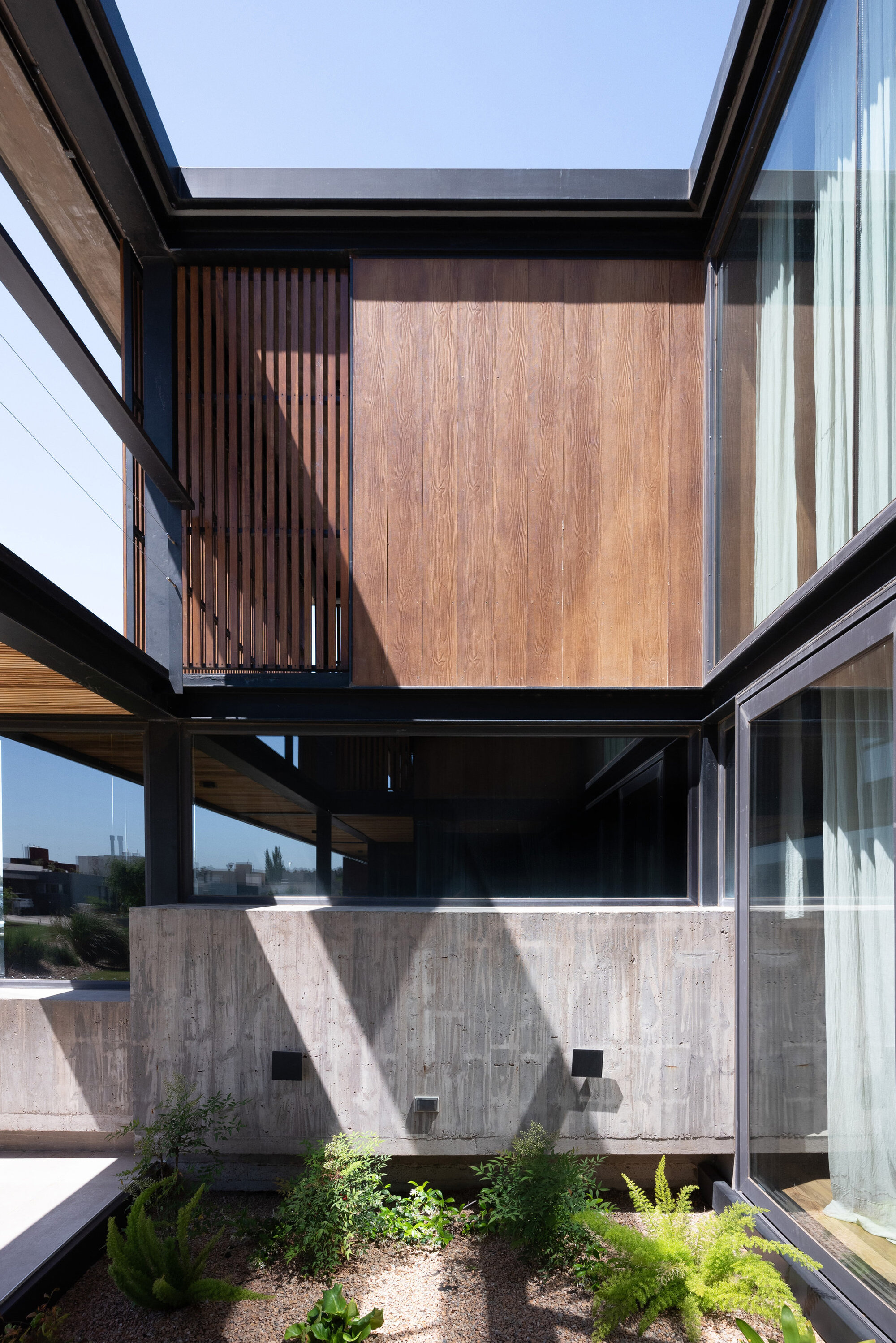 Interior courtyard with board-formed concrete walls and planted beds framed by steel beams and timber cladding above