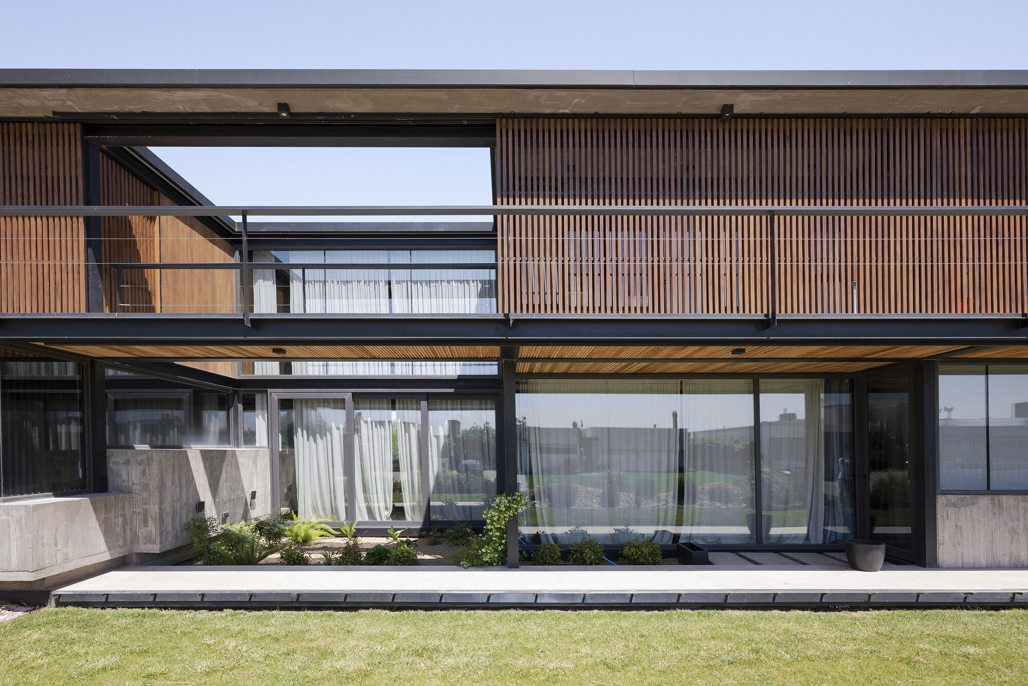 Garden facade showing stacked volumes with timber screens, concrete panels and planted terrace below an overcast sky