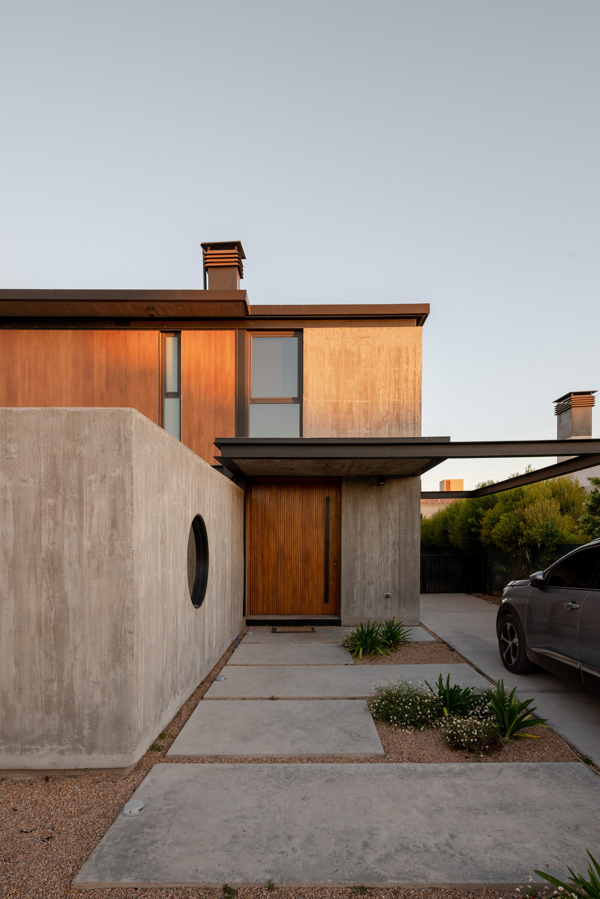 Entry facade with timber panels, concrete wall and circular porthole window at dusk