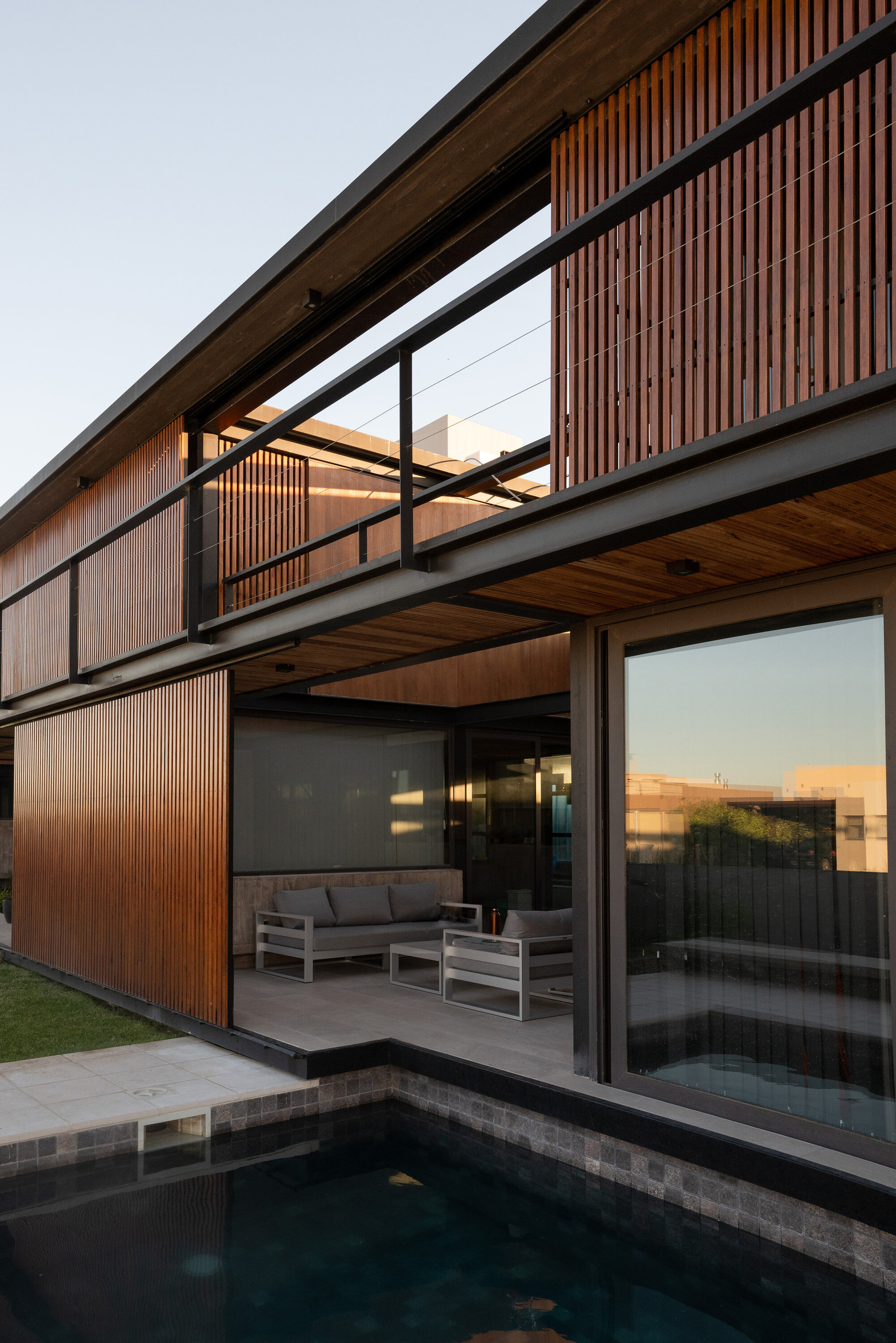 Poolside terrace with timber slat screens, black steel columns and slatted wood soffits at dusk