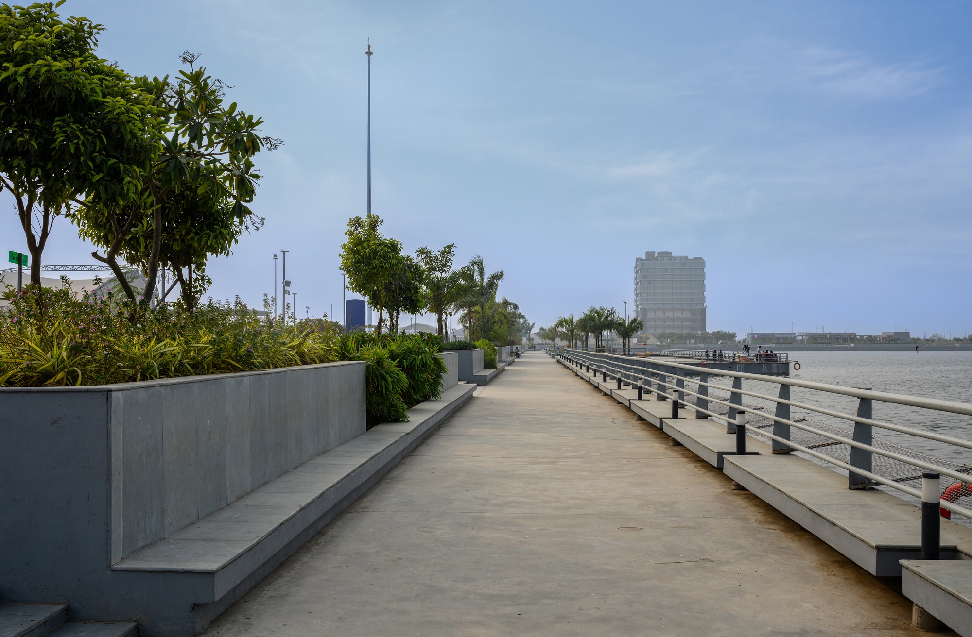Waterfront promenade with concrete planters and metal railings under clear daytime sky