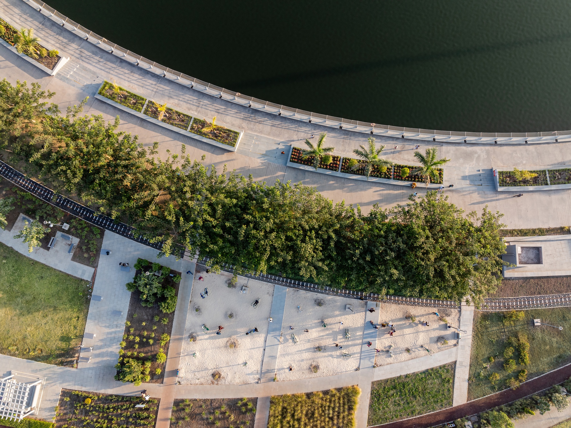 Drone view of the curved waterfront promenade with planted beds and pedestrians along the lake edge