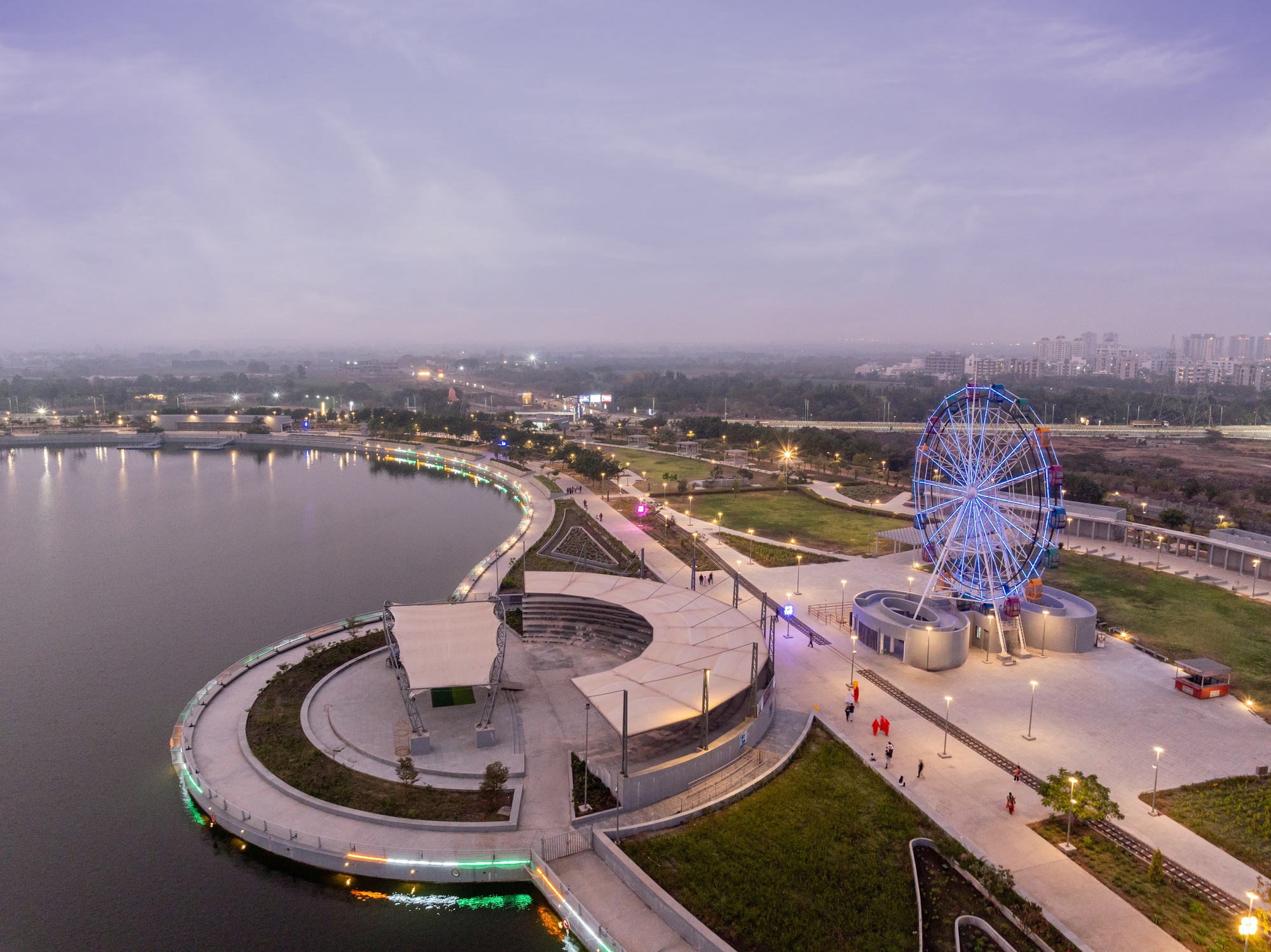 Circular pavilion with curved canopy and illuminated ferris wheel beside the waterfront at dusk