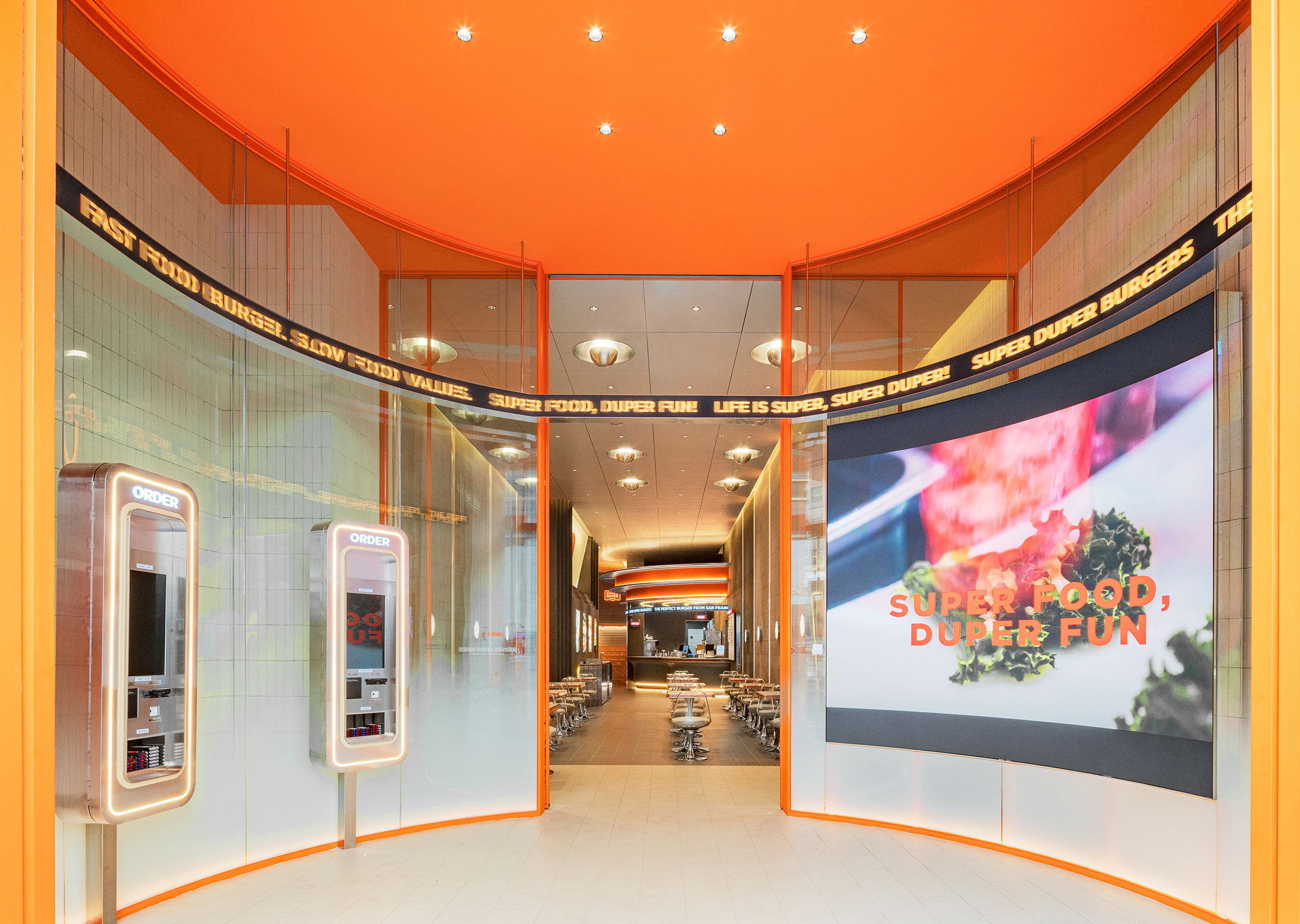 Entry vestibule with orange ceiling, glass walls, ordering kiosks, and view into dining area