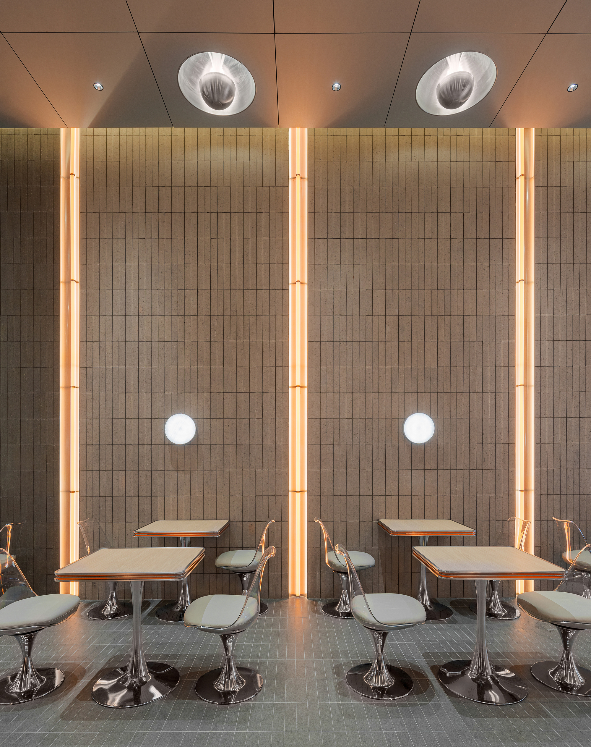 Dining area with fixed tables and chrome swivel chairs beneath vertical LED light strips