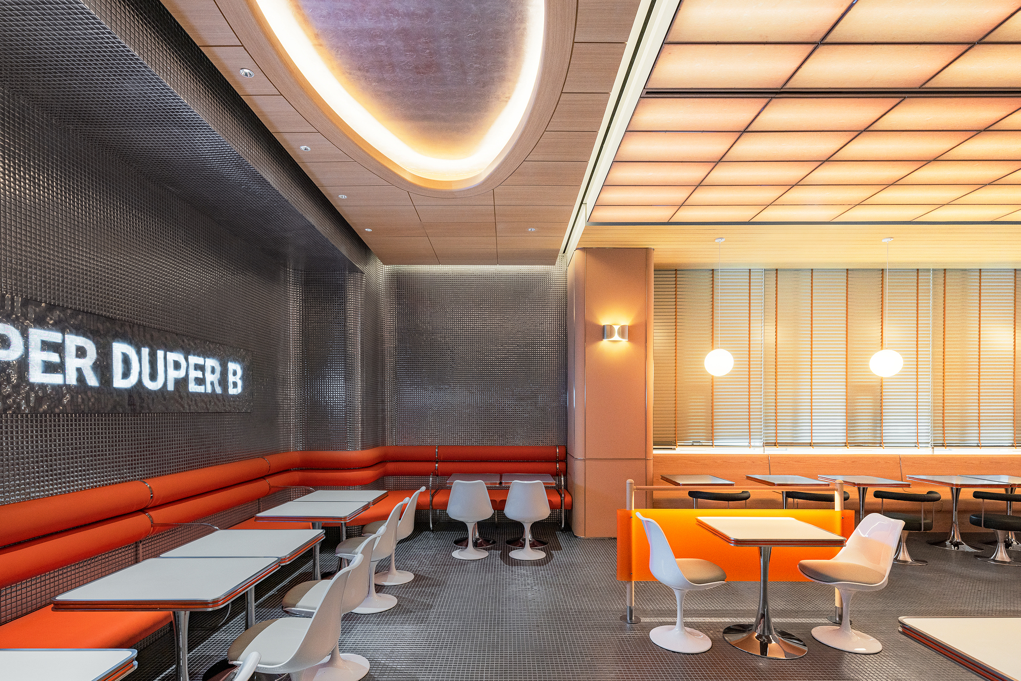 Curved banquette seating upholstered in orange vinyl against dark tiled wall with backlit ceiling cove