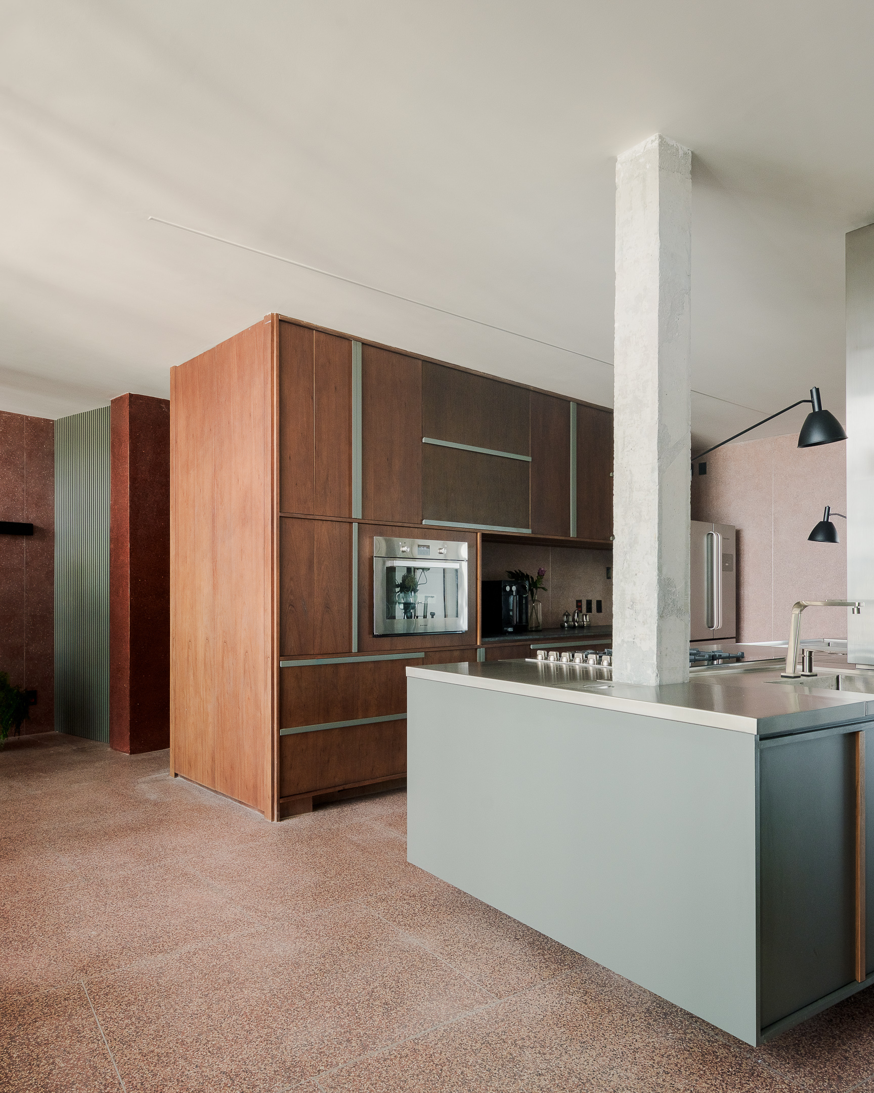 Open kitchen with pale island, timber cabinetry and exposed concrete column on terrazzo floor