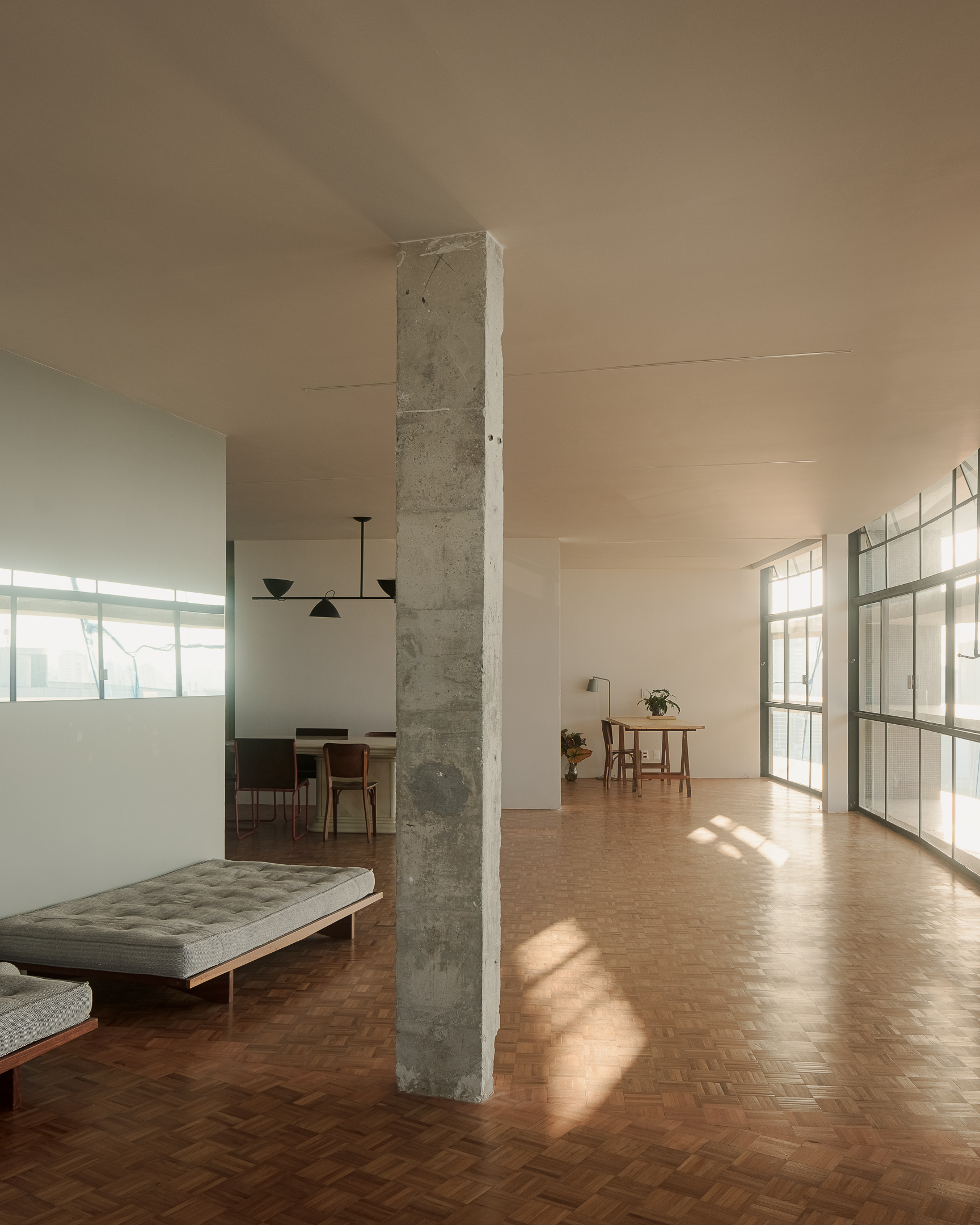 Open-plan interior with exposed concrete column dividing living and dining zones in warm afternoon light
