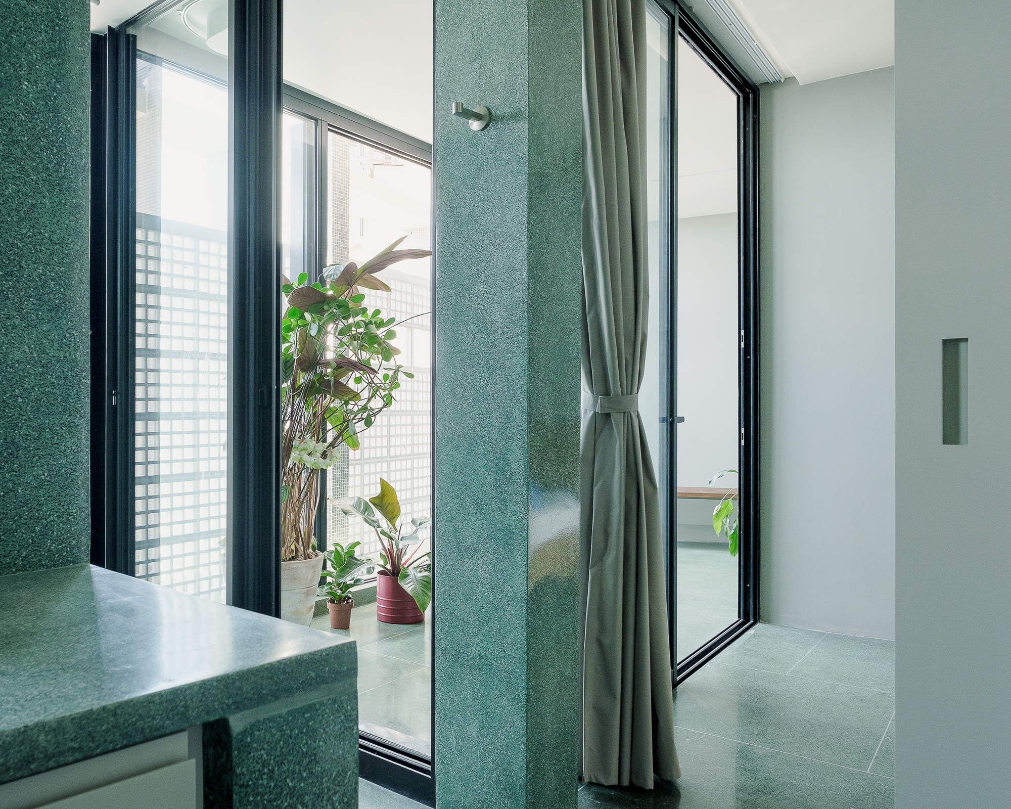 Bathroom corner with green terrazzo wall panels and black-framed windows opening to a planted balcony