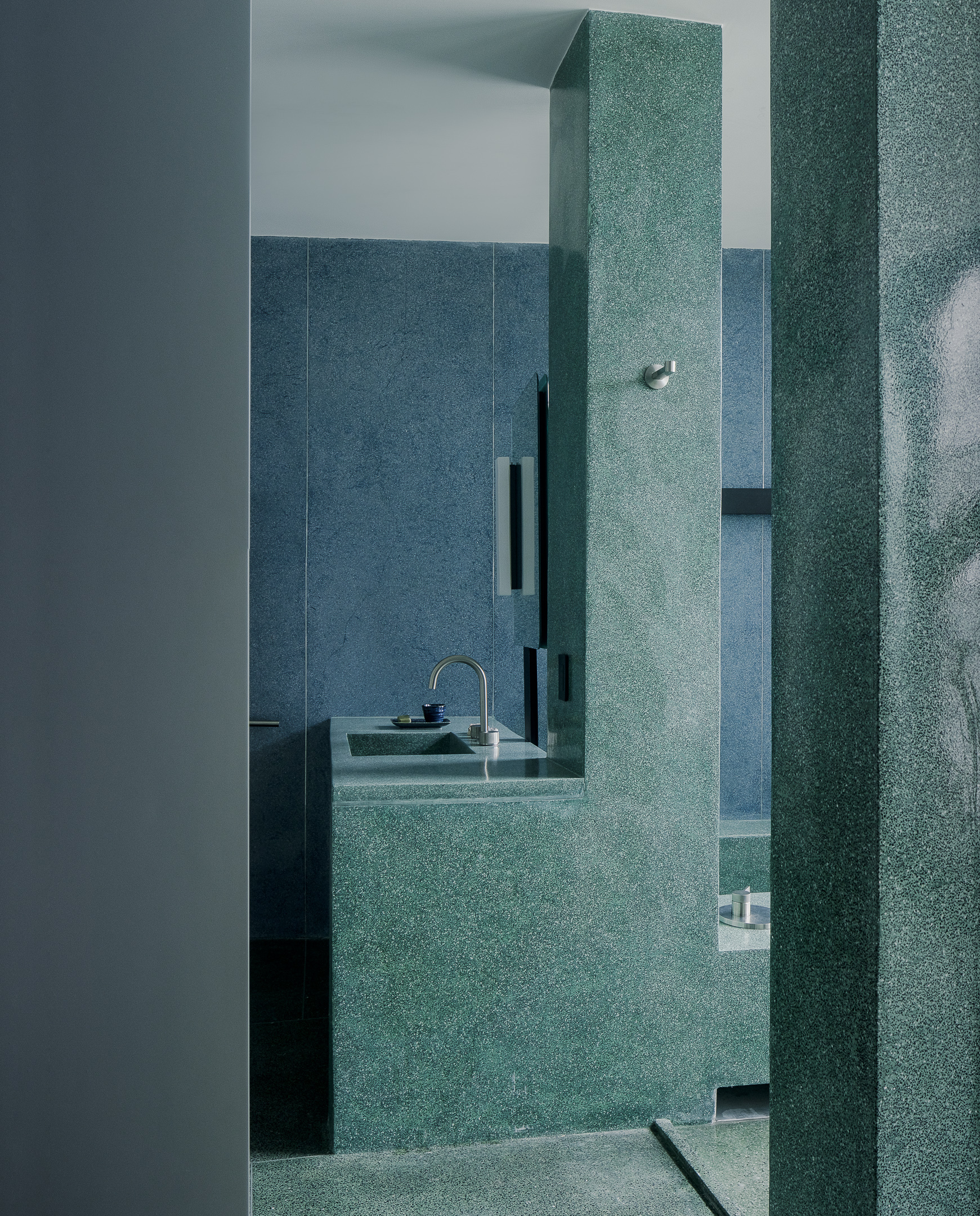 View through teal terrazzo columns into bathroom with floating sink and recessed black storage niches