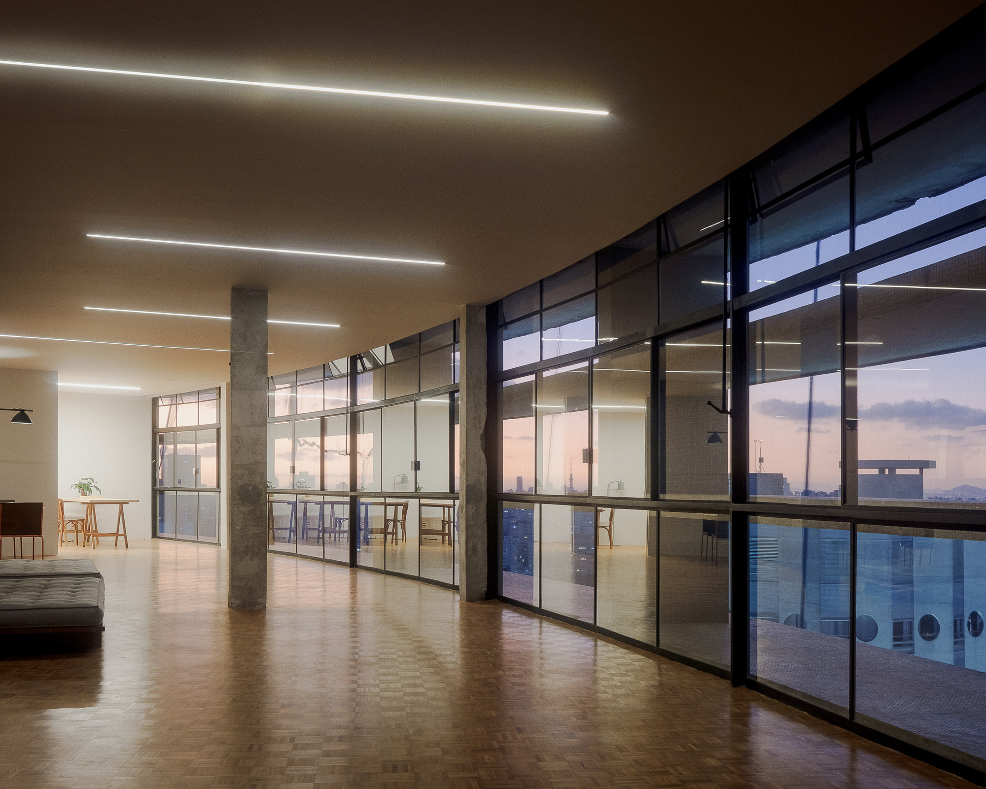 Steel-framed glazed partitions enclosing a terrace at dusk with city skyline beyond