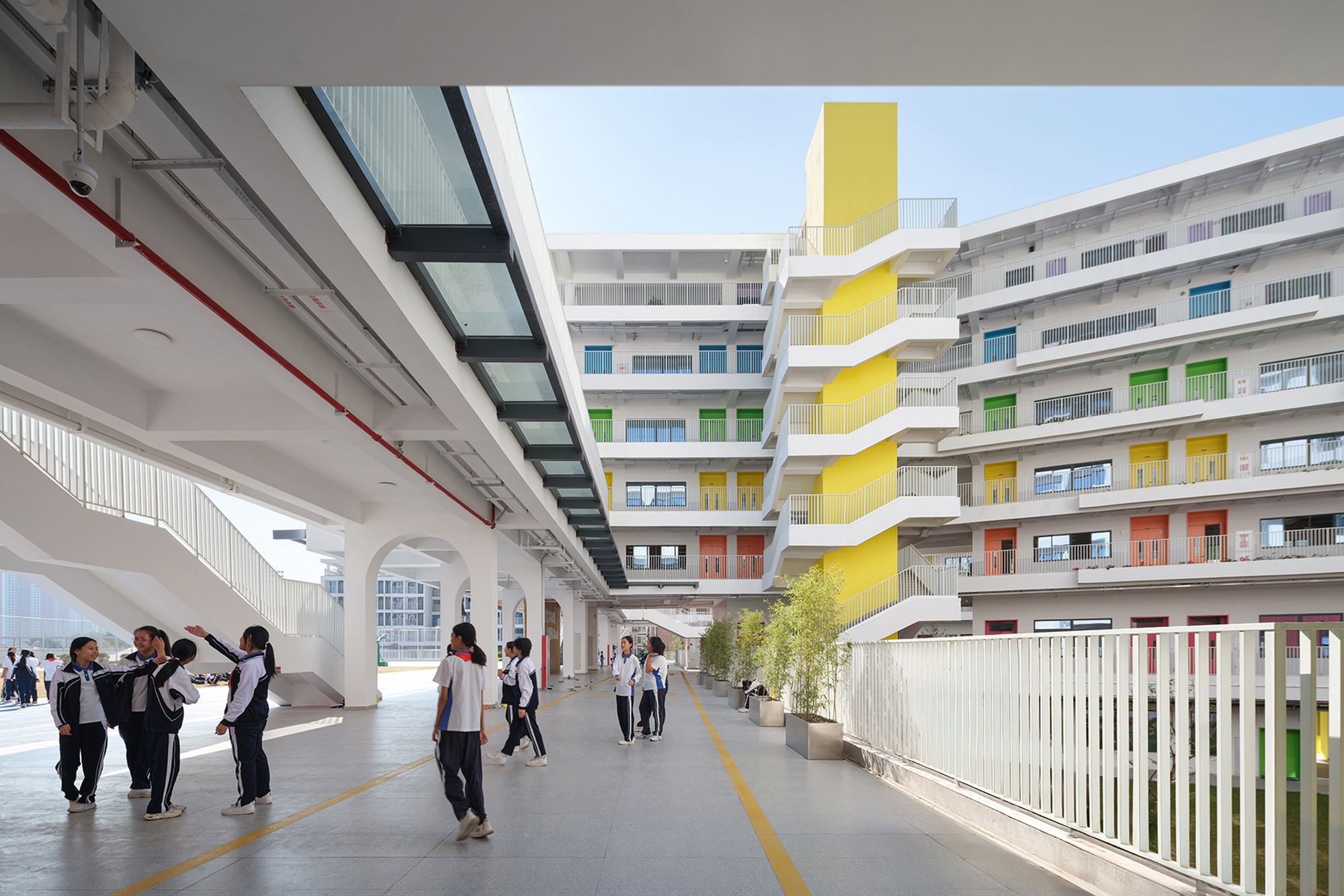 Covered corridor with white railings and students walking past coloured facade panels and planter boxes