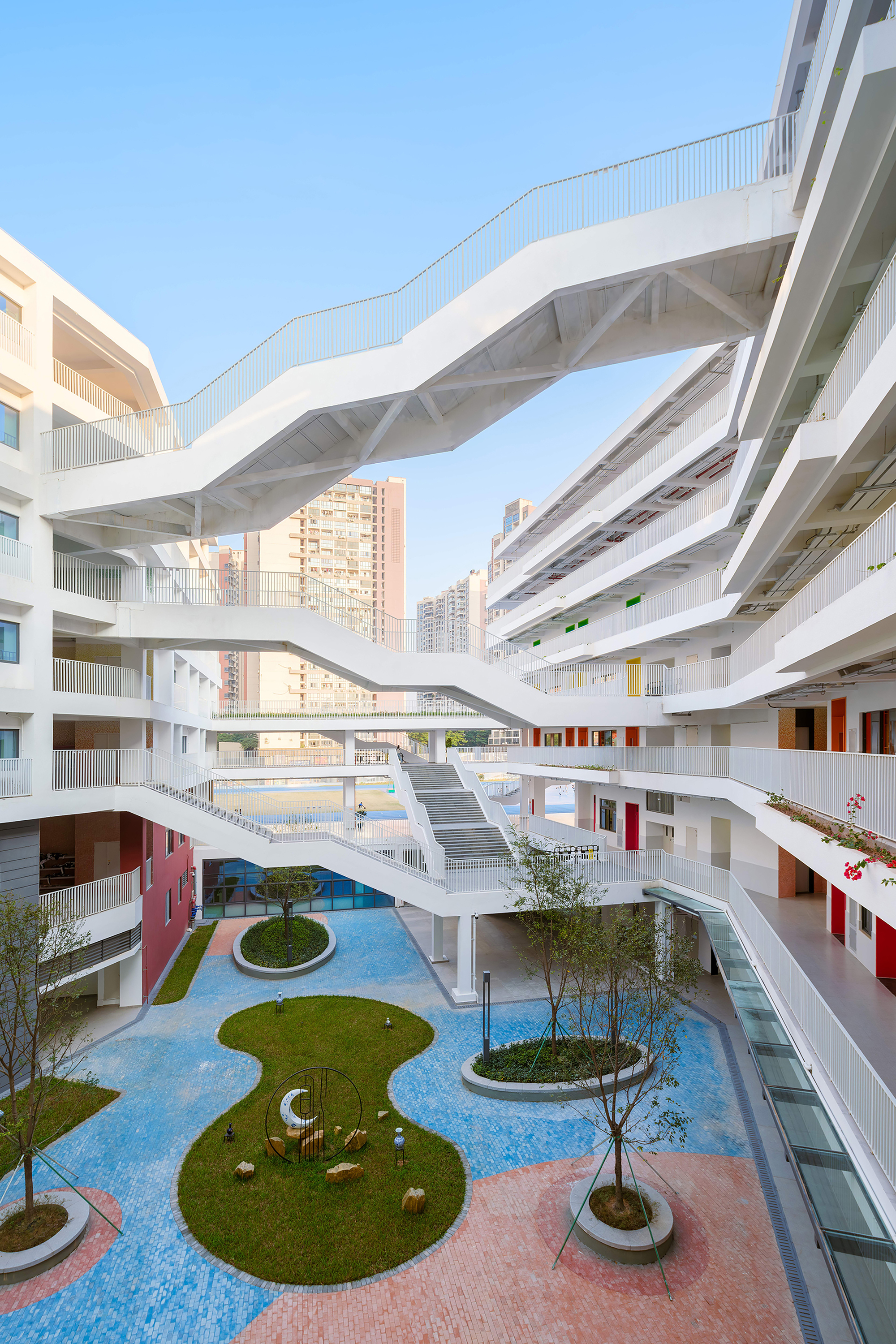 Courtyard with circular lawn planters in blue paving and white bridges connecting multilevel building facades