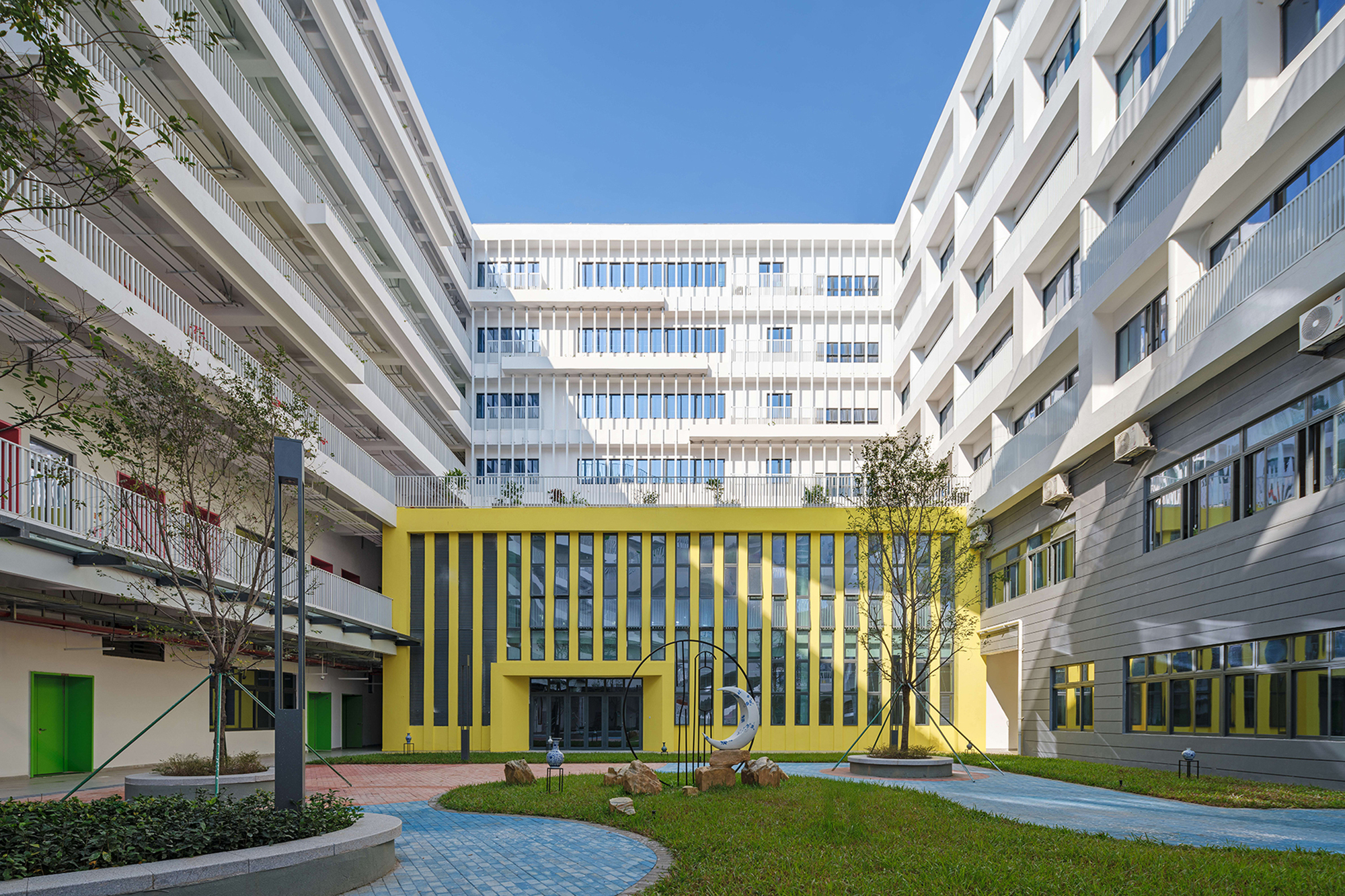 Courtyard with yellow vertical fin facade flanked by white striped buildings and young trees on lawn