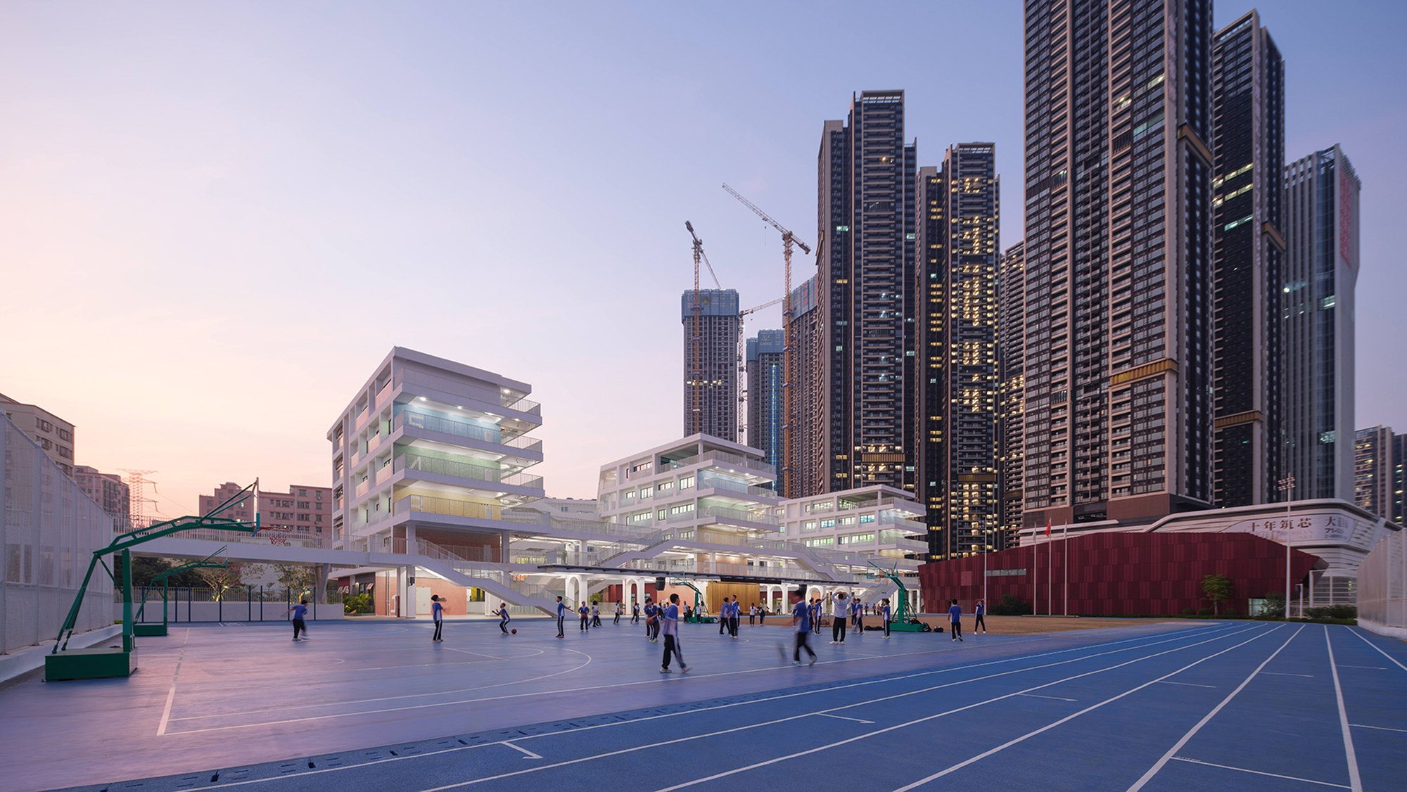 Wide view of the school campus with illuminated facades and students on the sports court at twilight