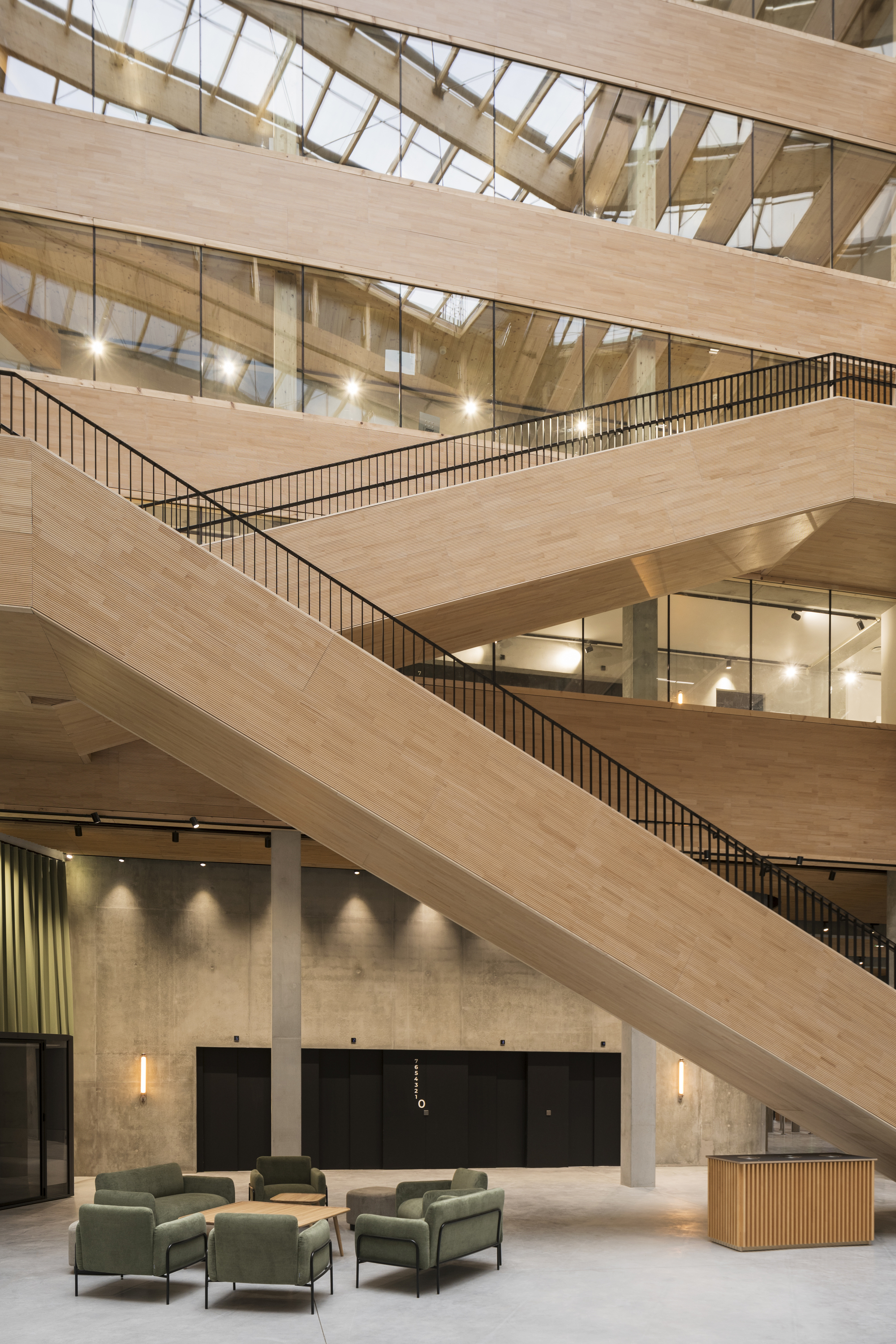 Interior atrium with stacked timber-clad balconies and metal railings under a glazed skylight