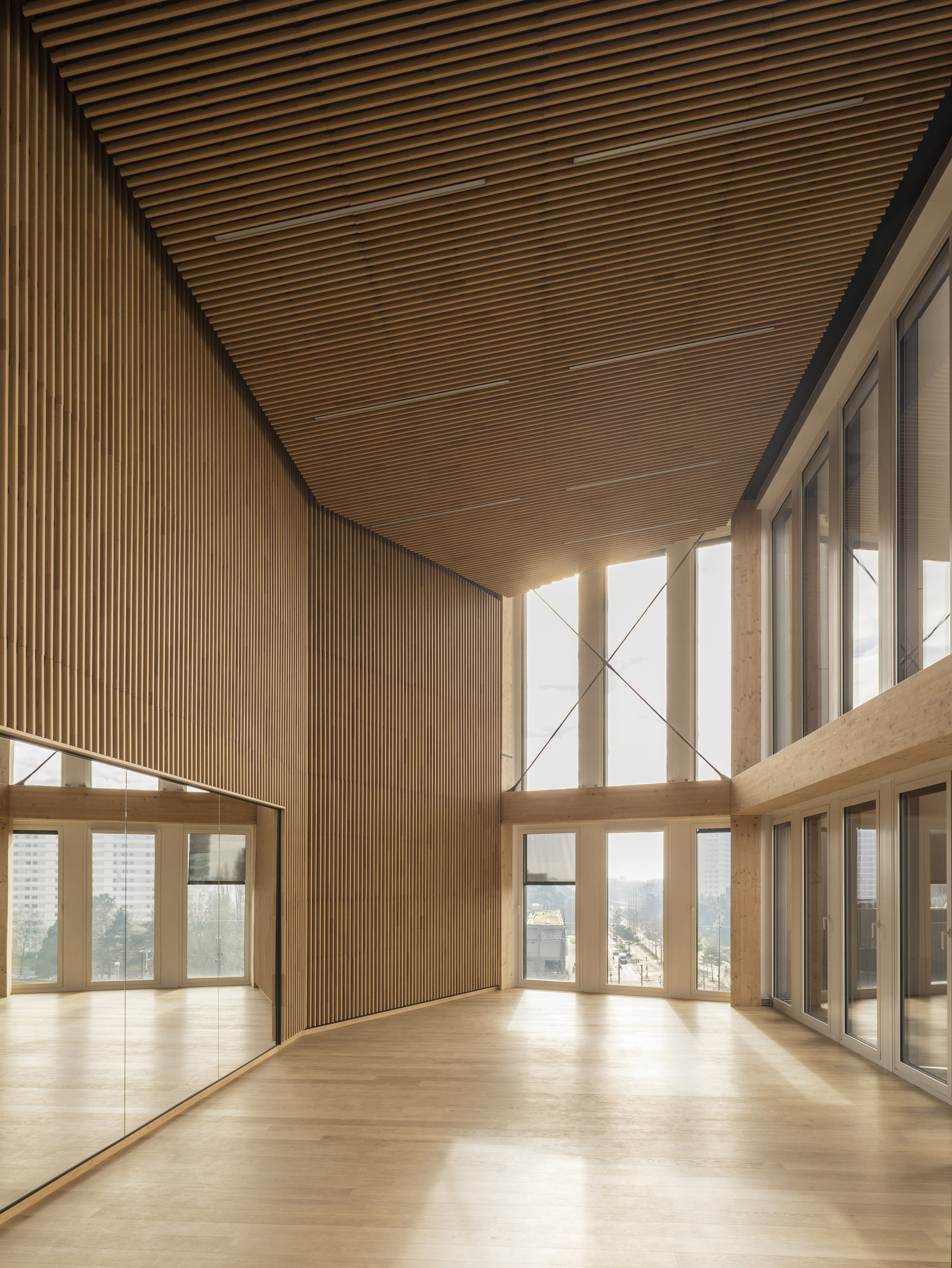 Double-height space with slatted timber ceiling and floor-to-ceiling windows overlooking the cityscape