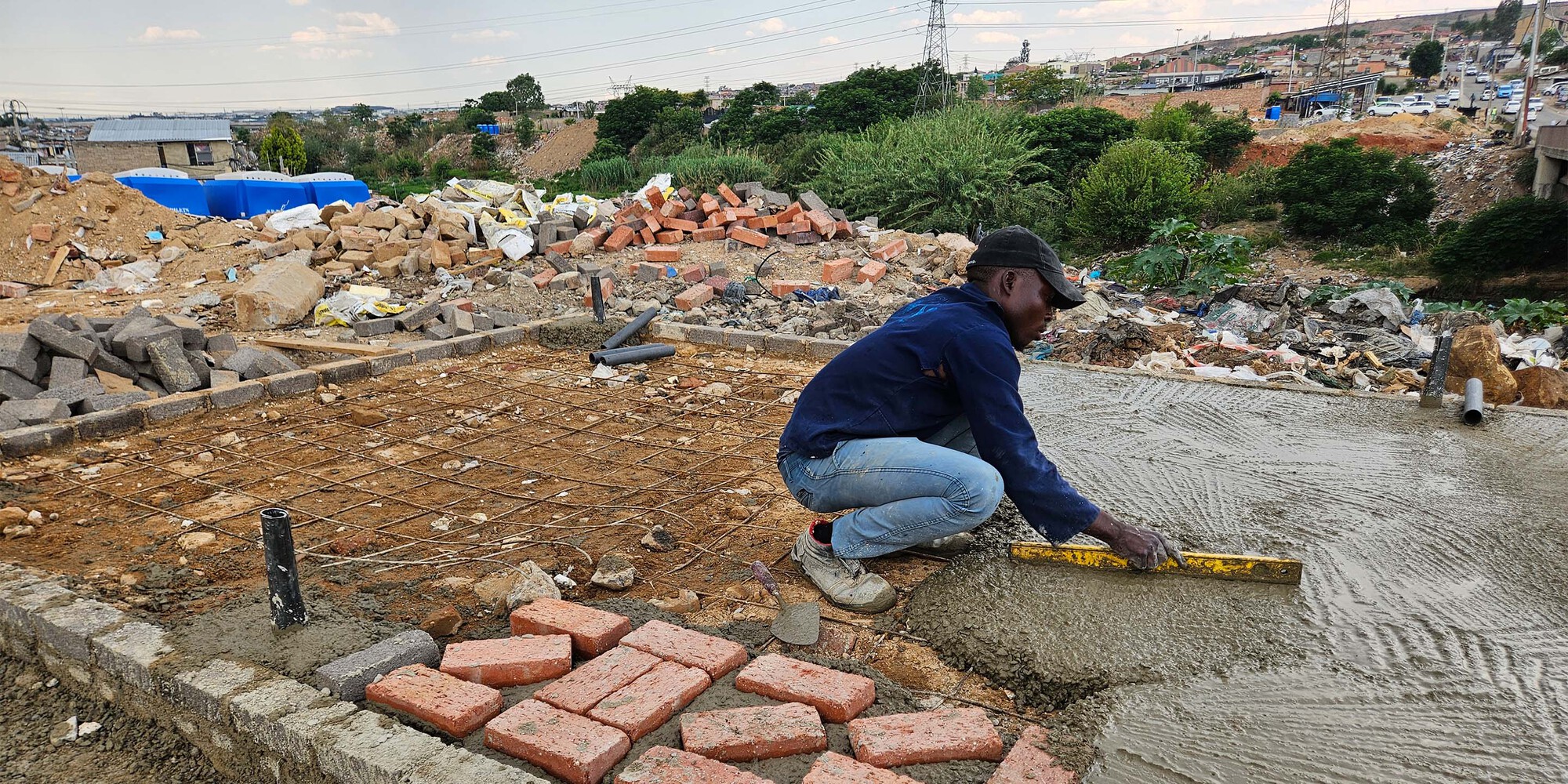 Worker smoothing a fresh concrete slab with red bricks laid out at the edge of the formwork