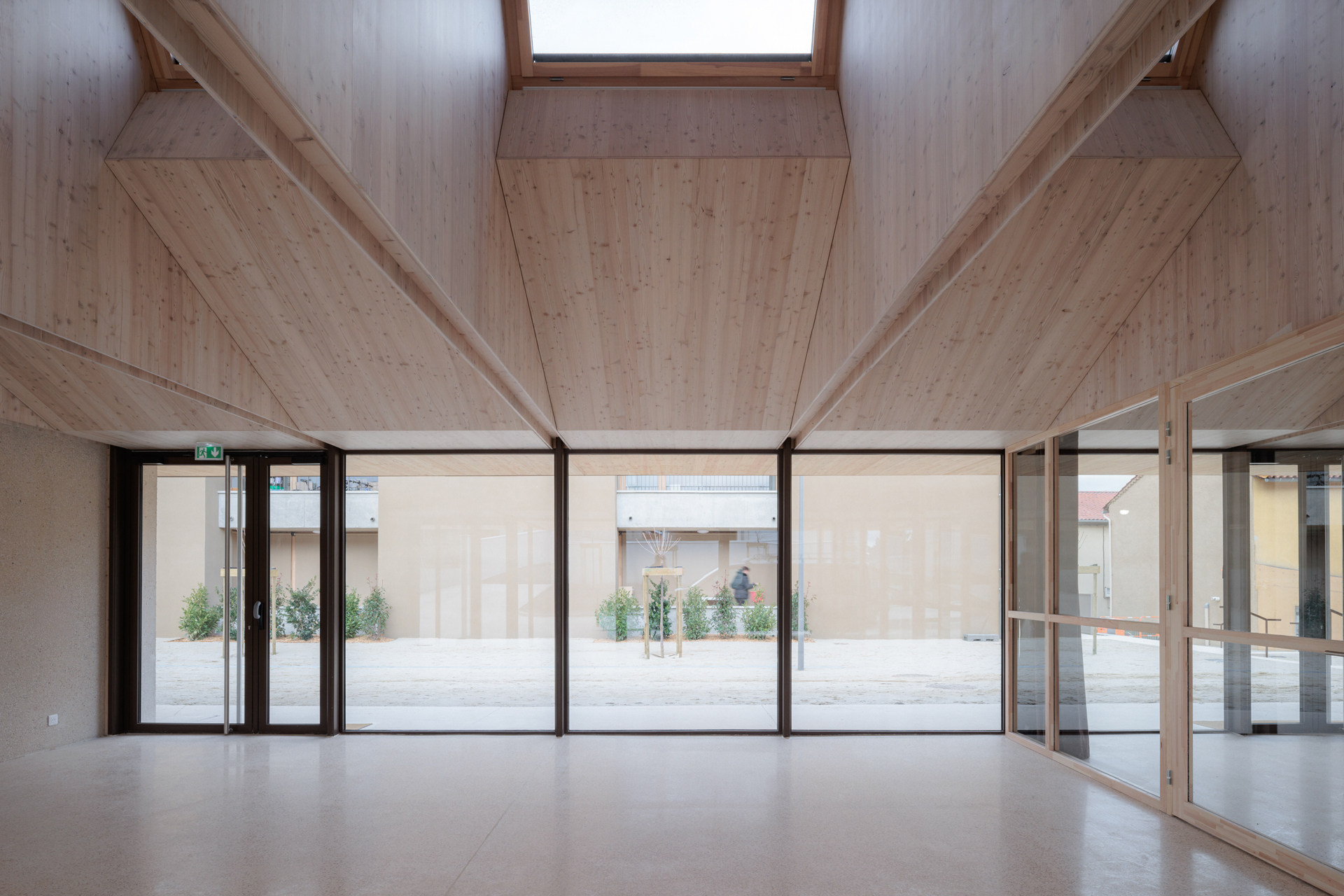 Interior space with exposed timber ceiling beams and full-height glazing overlooking an exterior courtyard