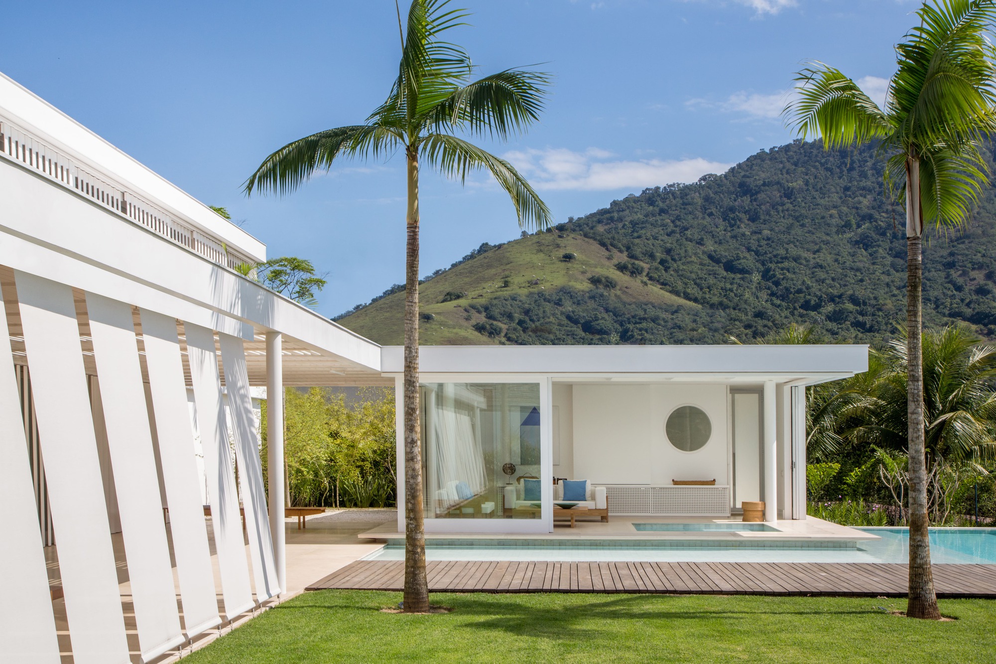 Glass pavilion with recessed lounge overlooking the pool and forested hillside in the distance