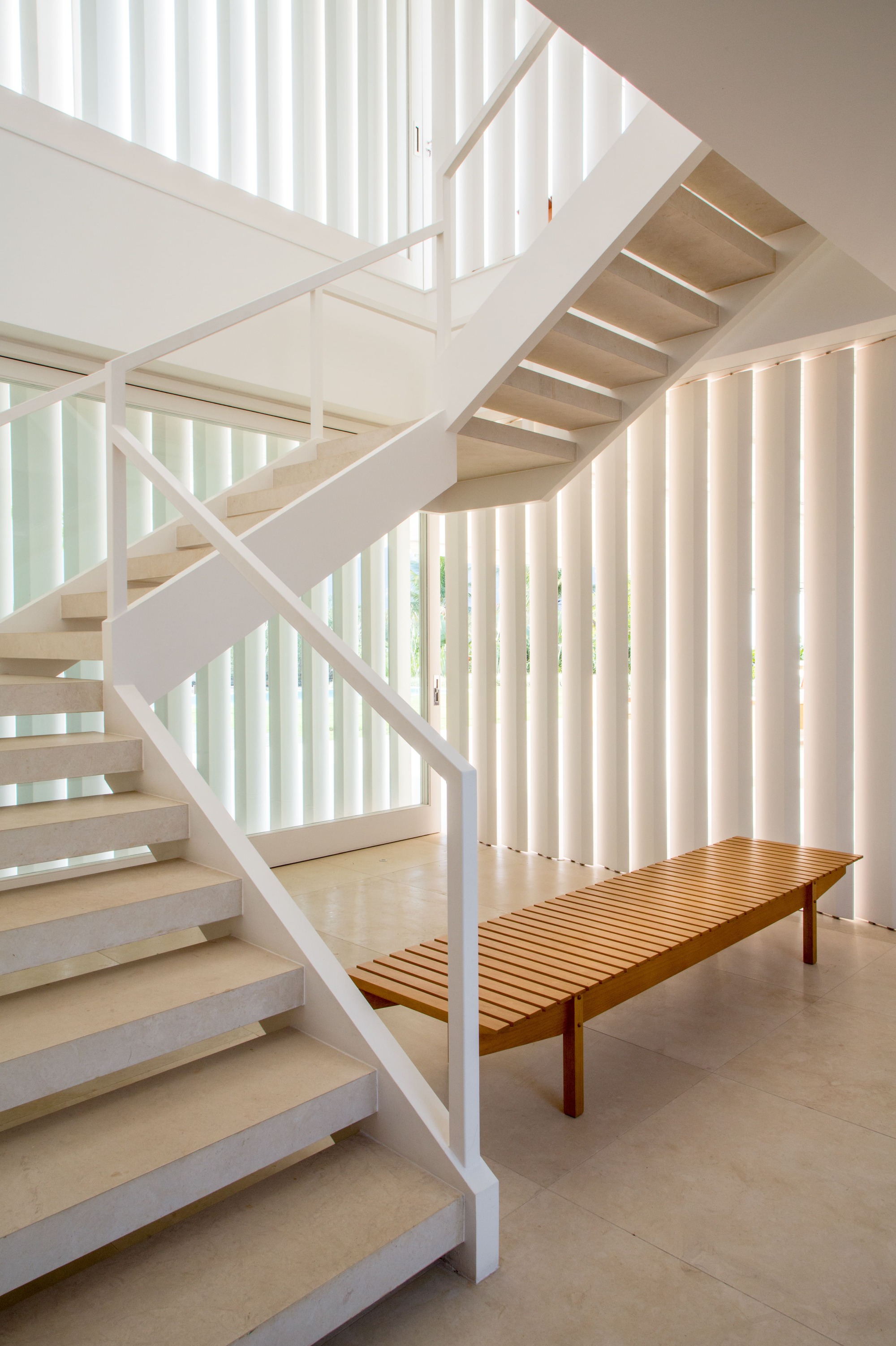 White steel staircase with open treads beside vertical slat screens and a slatted timber bench