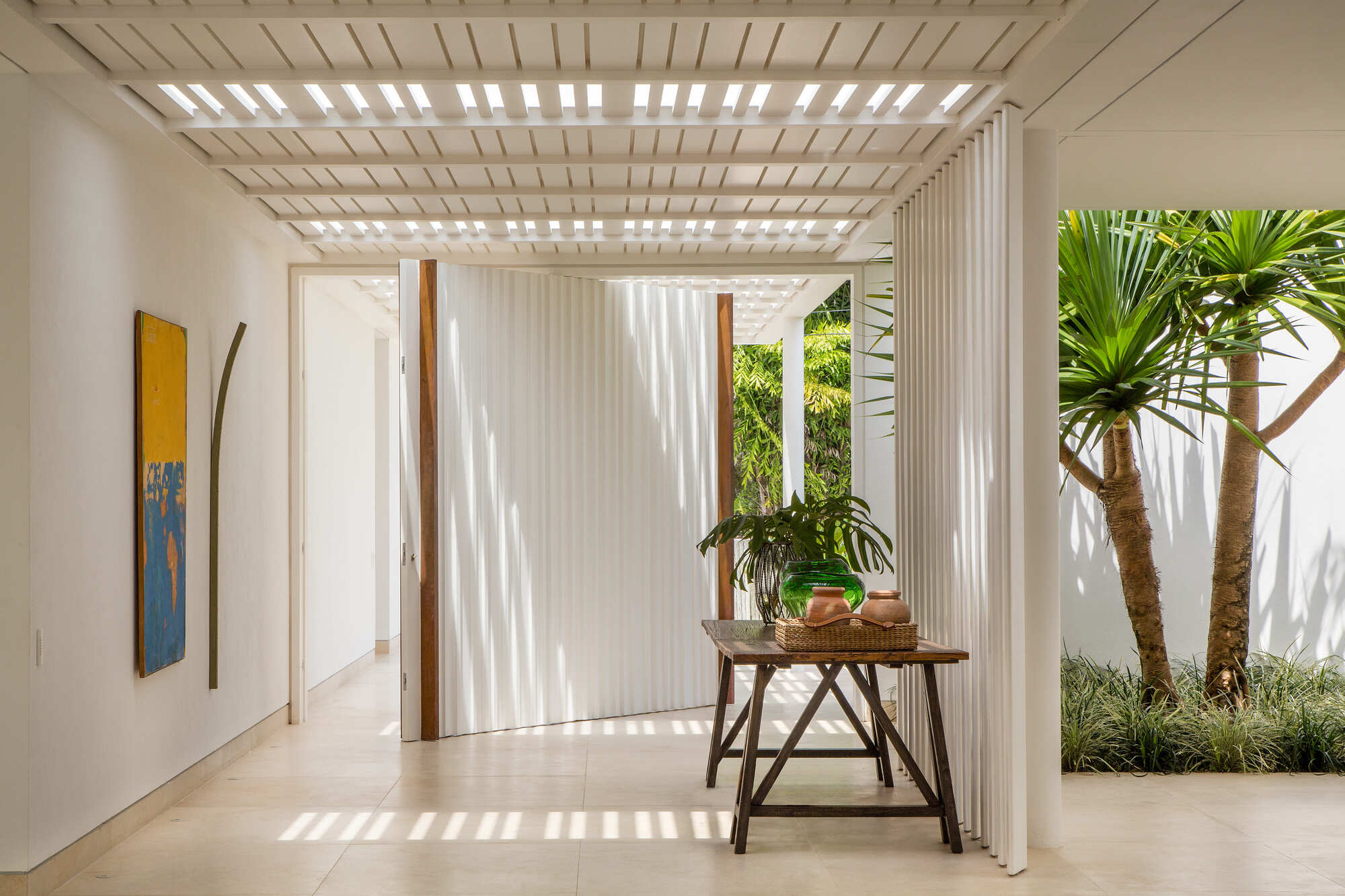 Interior courtyard with slatted timber pergola casting shadows over potted plants and palm trunks