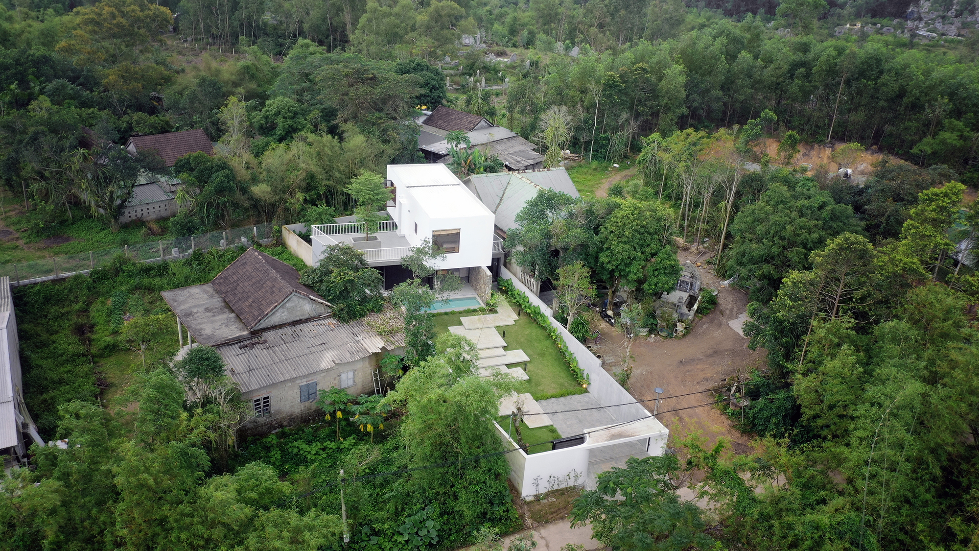 Aerial view showing the white volumes and swimming pool nestled among dense tropical vegetation and neighboring houses