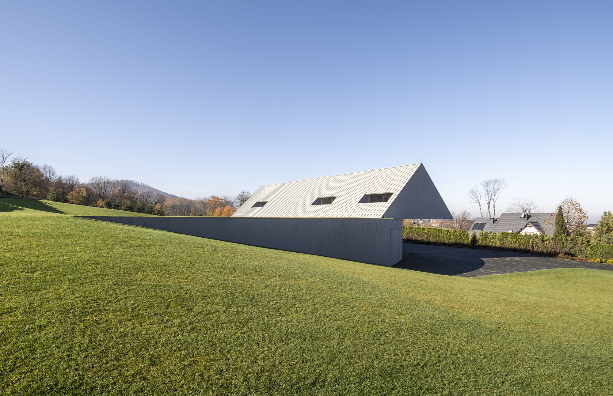 Side elevation showing the ribbed metal roof and dark facade against rolling hills in autumn