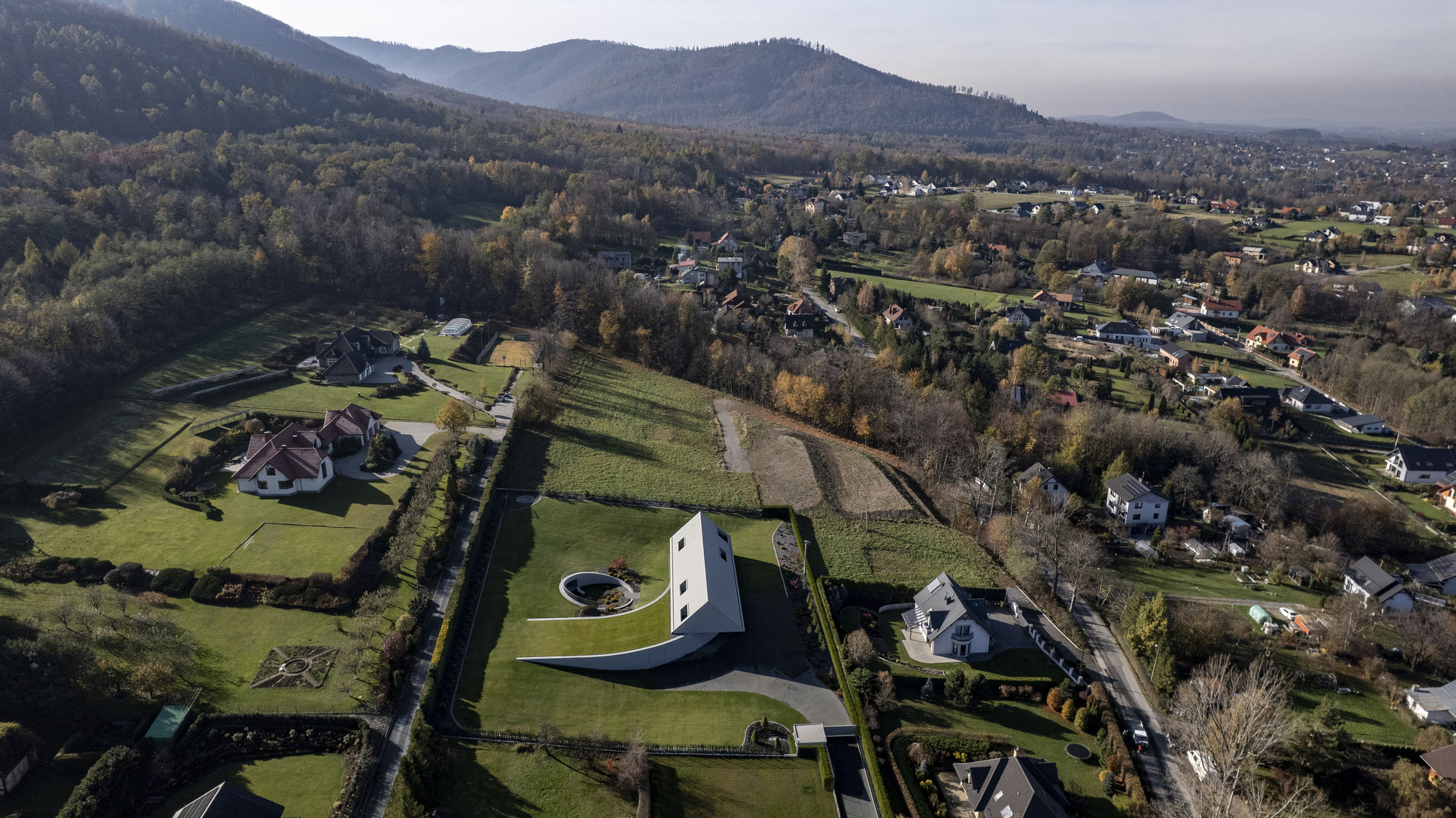 Drone view of the residence set among fields and forested hills at dawn