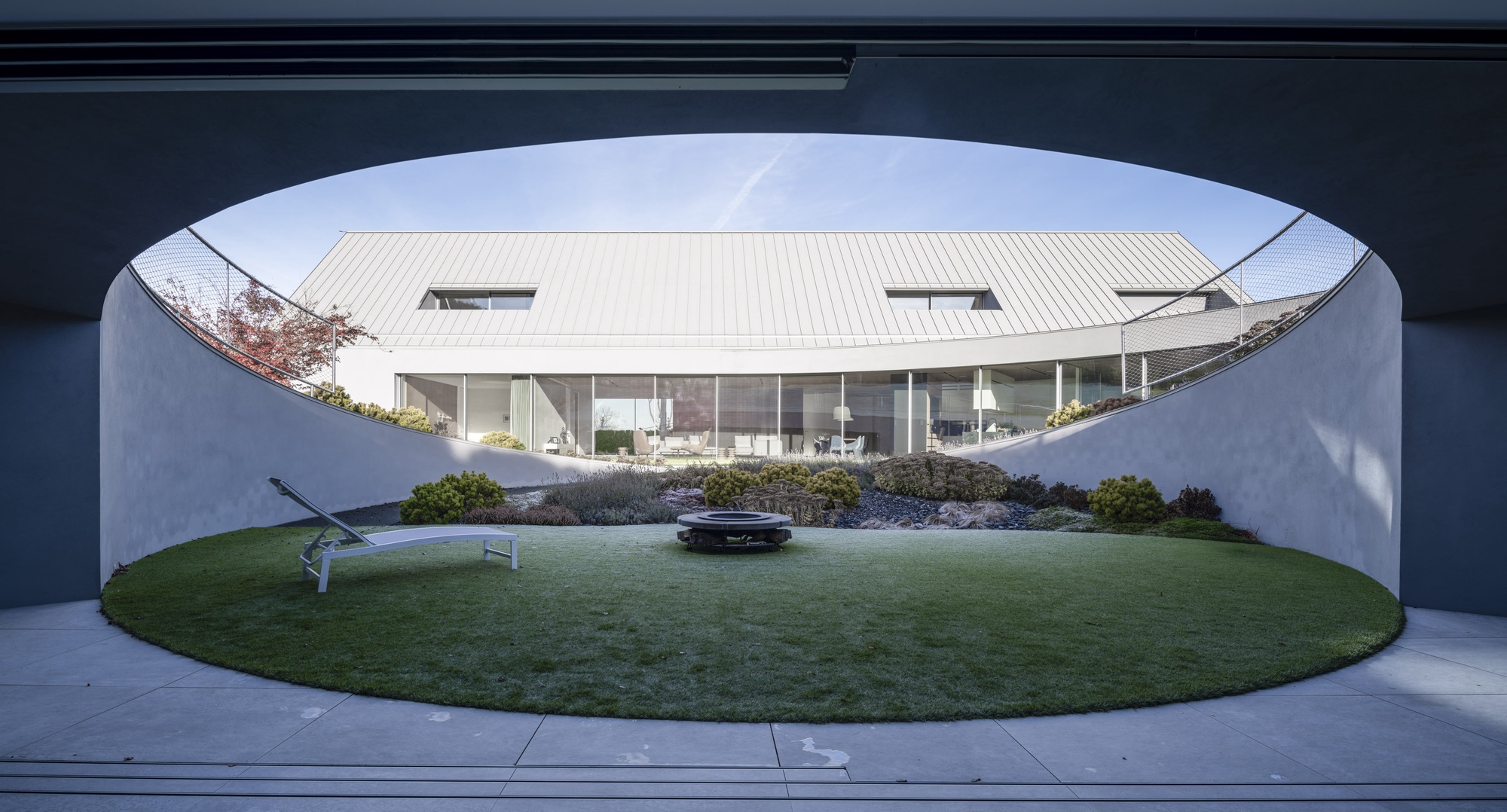 View through arched concrete portal onto glass-walled living space and circular lawn courtyard below