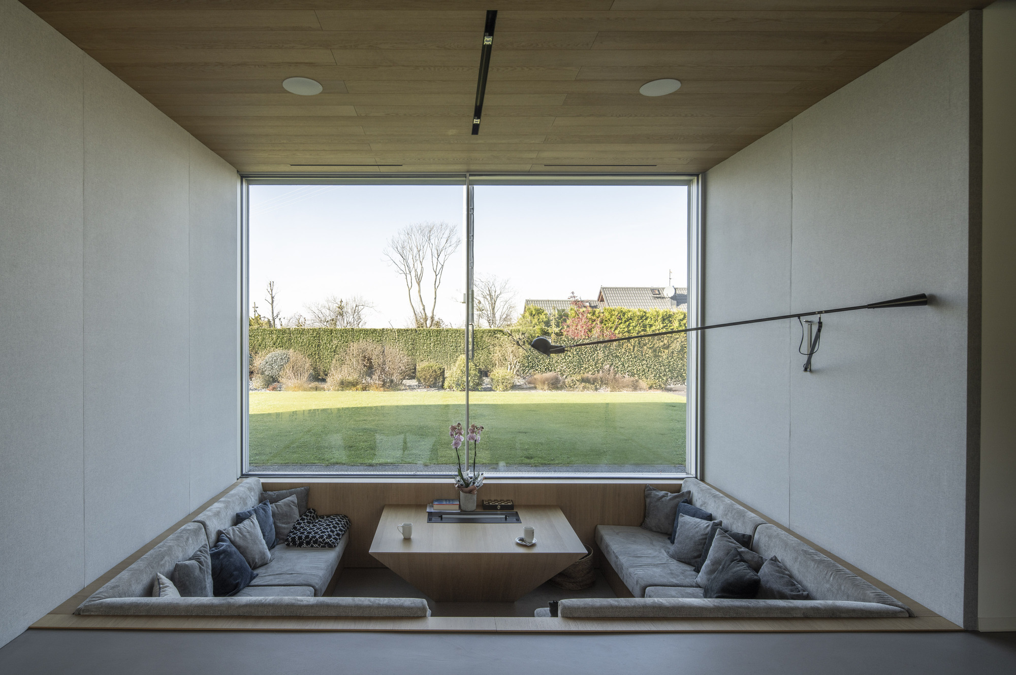 Sunken seating pit with upholstered benches framed by timber and glass walls overlooking the lawn