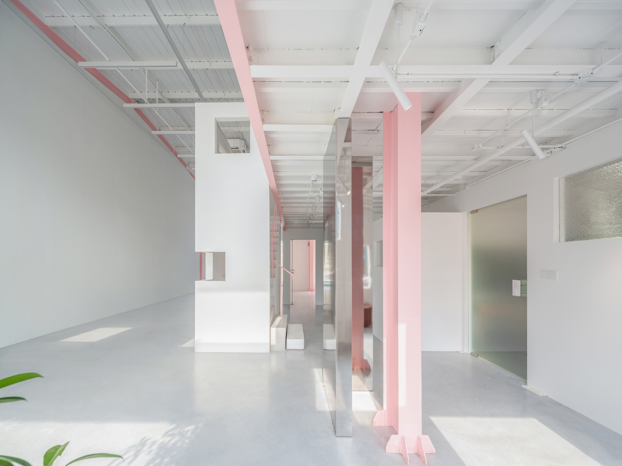 Interior view with pink structural columns and white partition walls beneath translucent corrugated ceiling