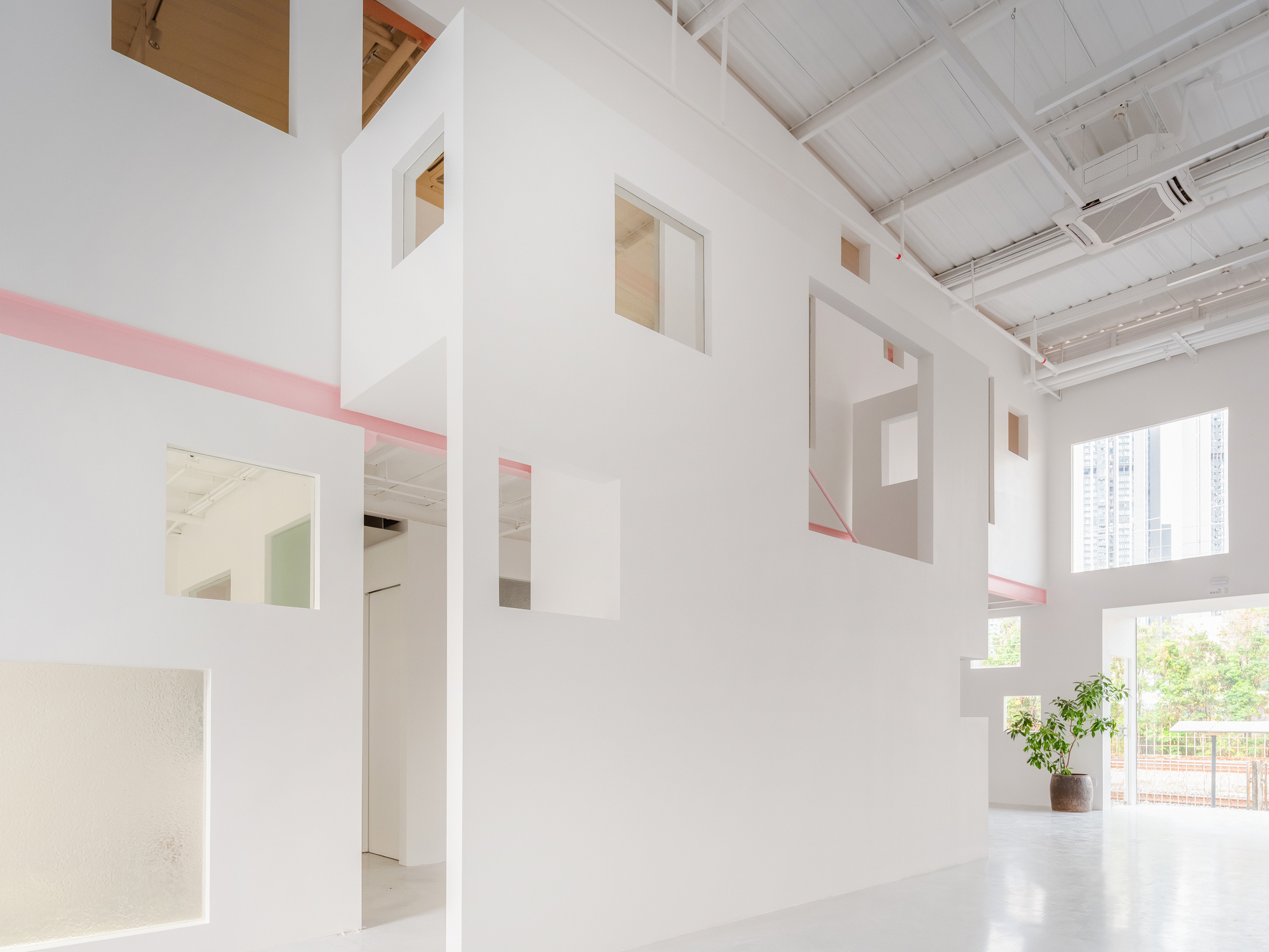 White interior partition with cut-out openings and pink steel trim beneath a sawtooth skylight