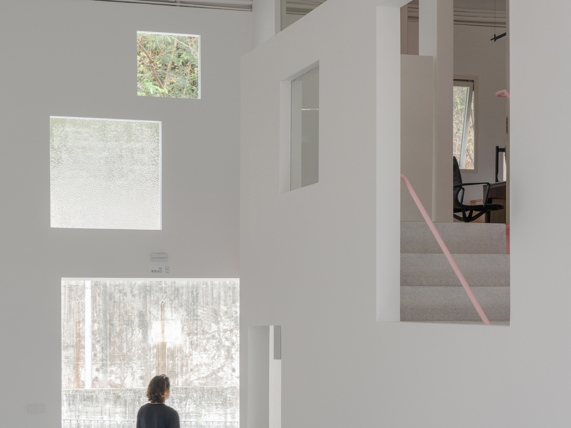 Person standing before three vertically stacked windows with translucent and clear glass overlooking winter trees