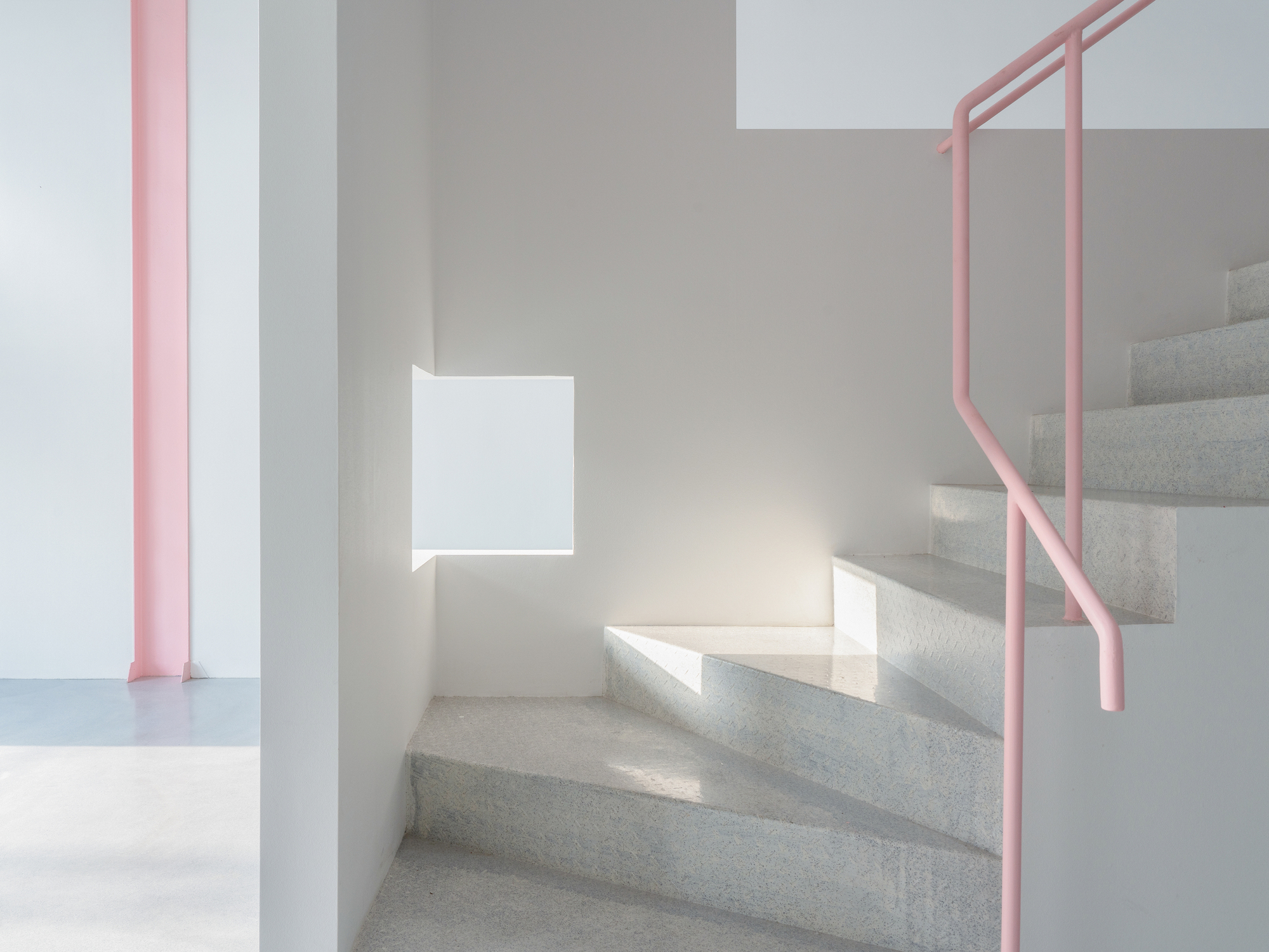 Terrazzo staircase with pink tubular handrail and sunlight casting shadows on white walls