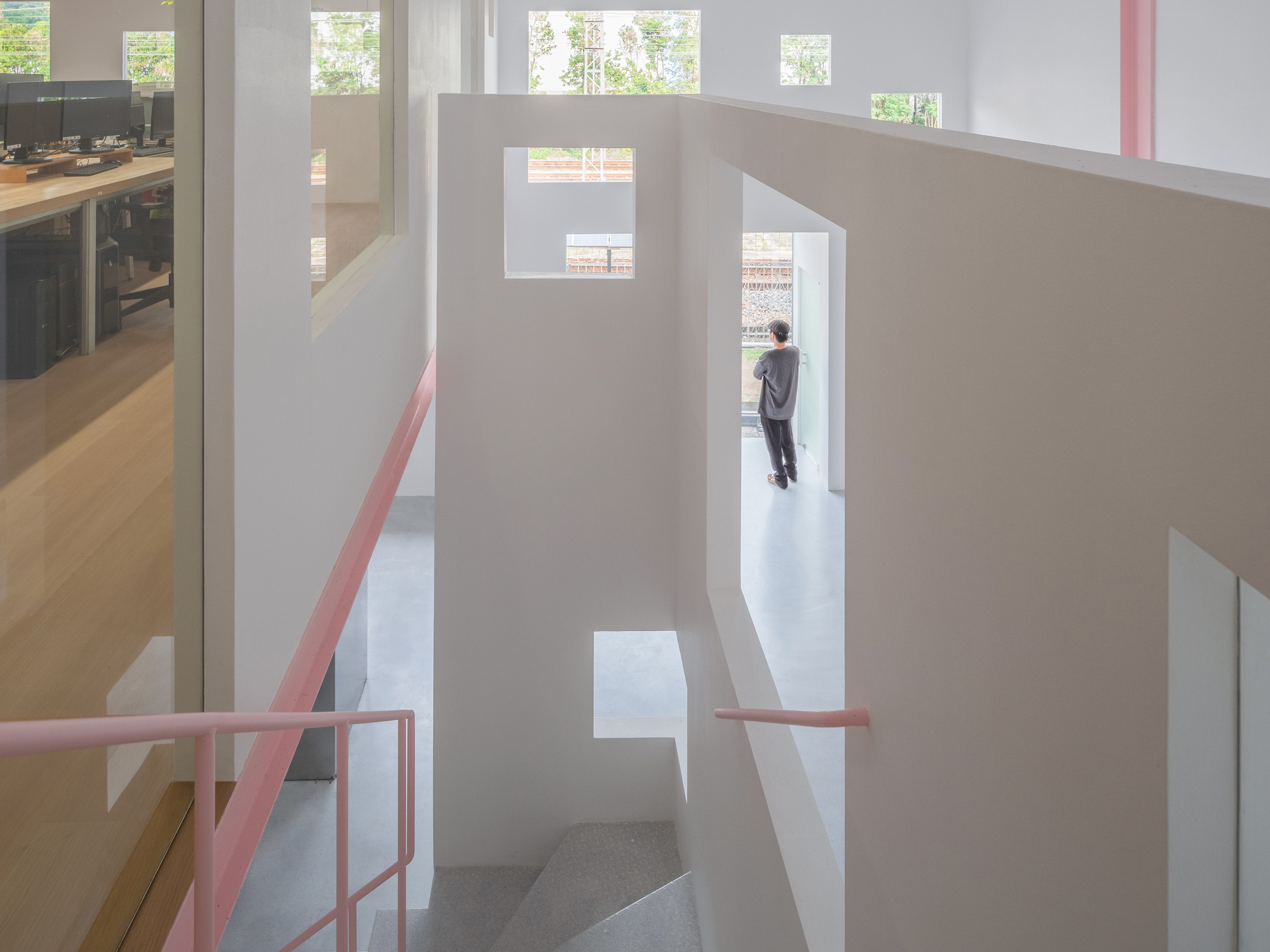 Multi-level interior with a lone figure standing in a doorway framed by tall white partitions