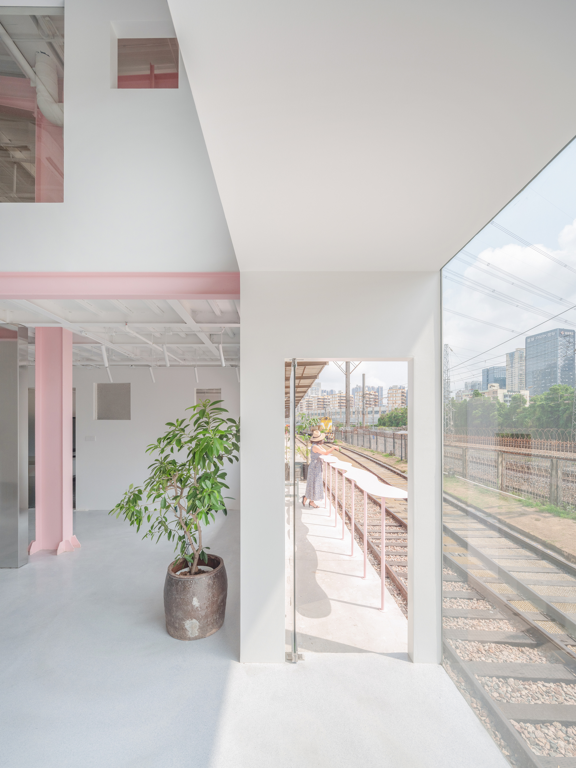 Interior opening to an exterior balcony overlooking railway tracks with a potted tree in foreground
