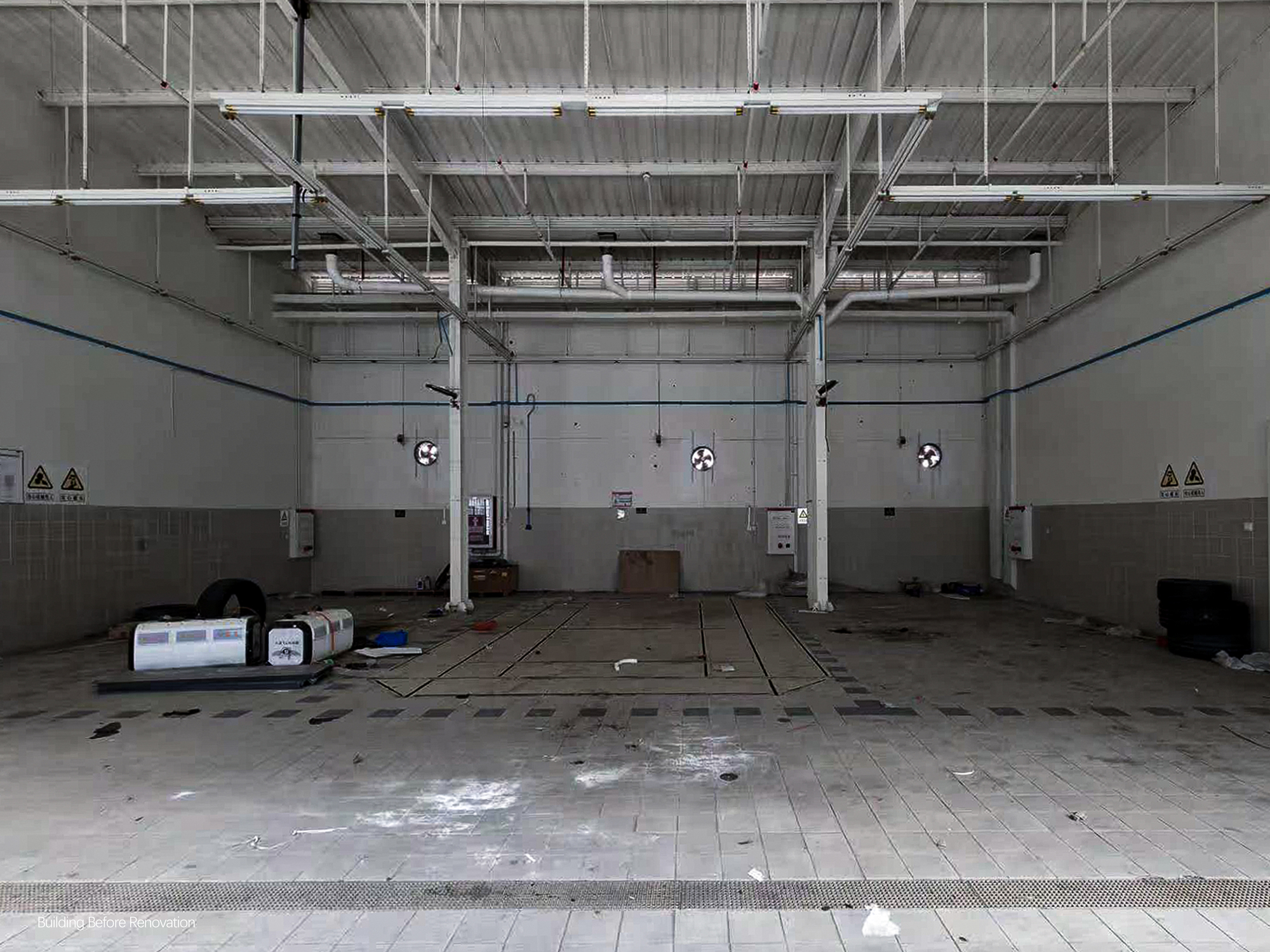 Interior of a garage bay with exposed ceiling ducts and wet concrete floor