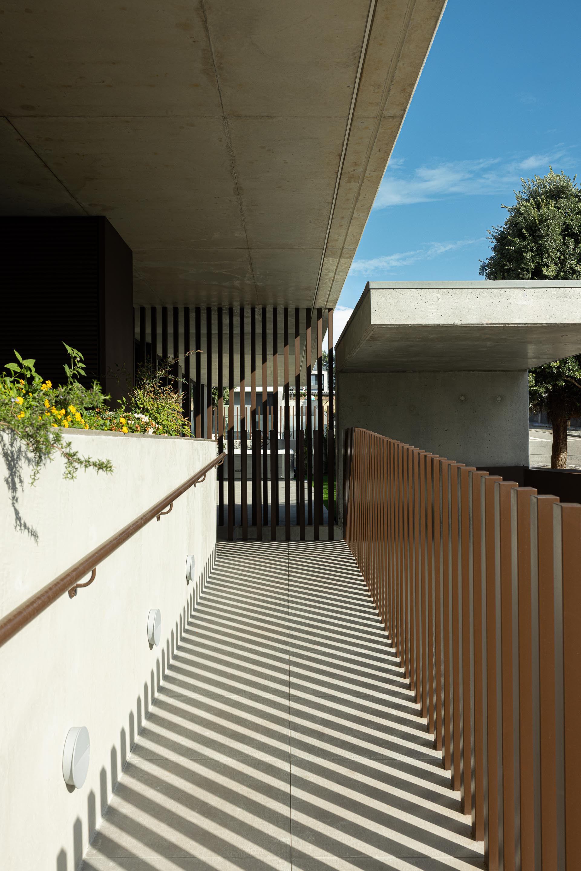 Outdoor corridor with vertical timber slat screen casting shadows on white walls and concrete soffit