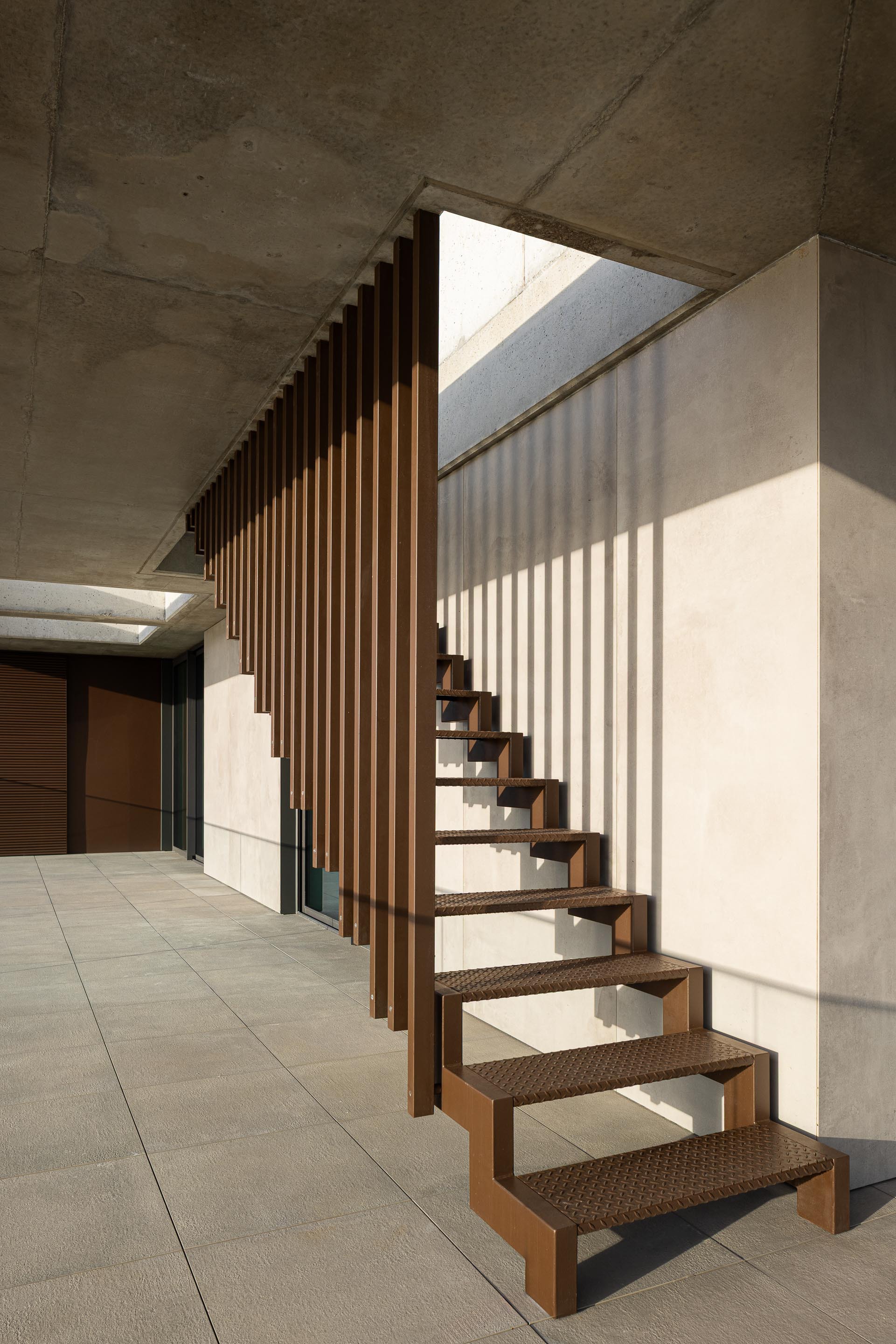 Timber staircase with open risers beneath an angled concrete ceiling and skylight casting shadows