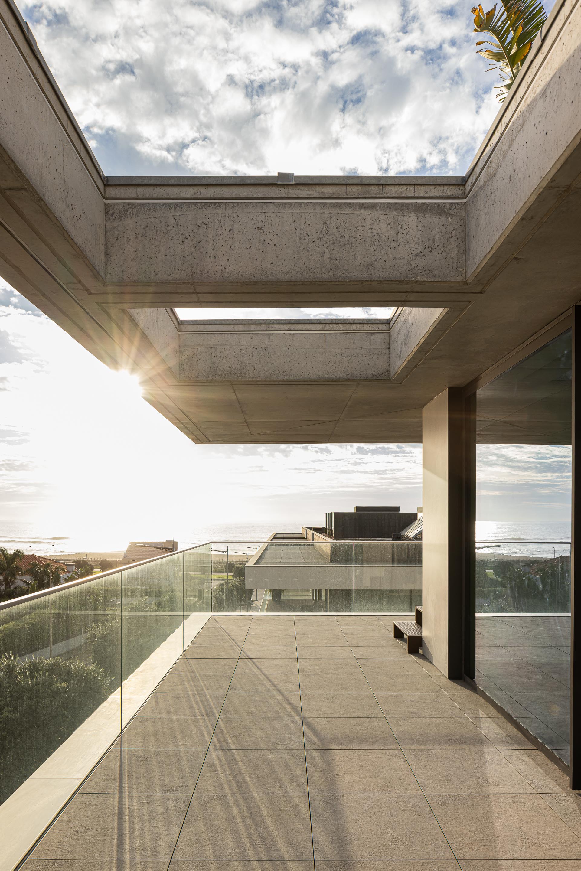 Open terrace with concrete soffits and skylights framing a distant ocean view under partly cloudy skies