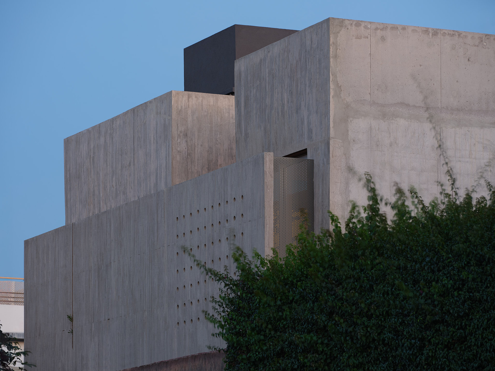Corner detail of the layered concrete volumes with perforated panel and perforated metal vent opening at dusk