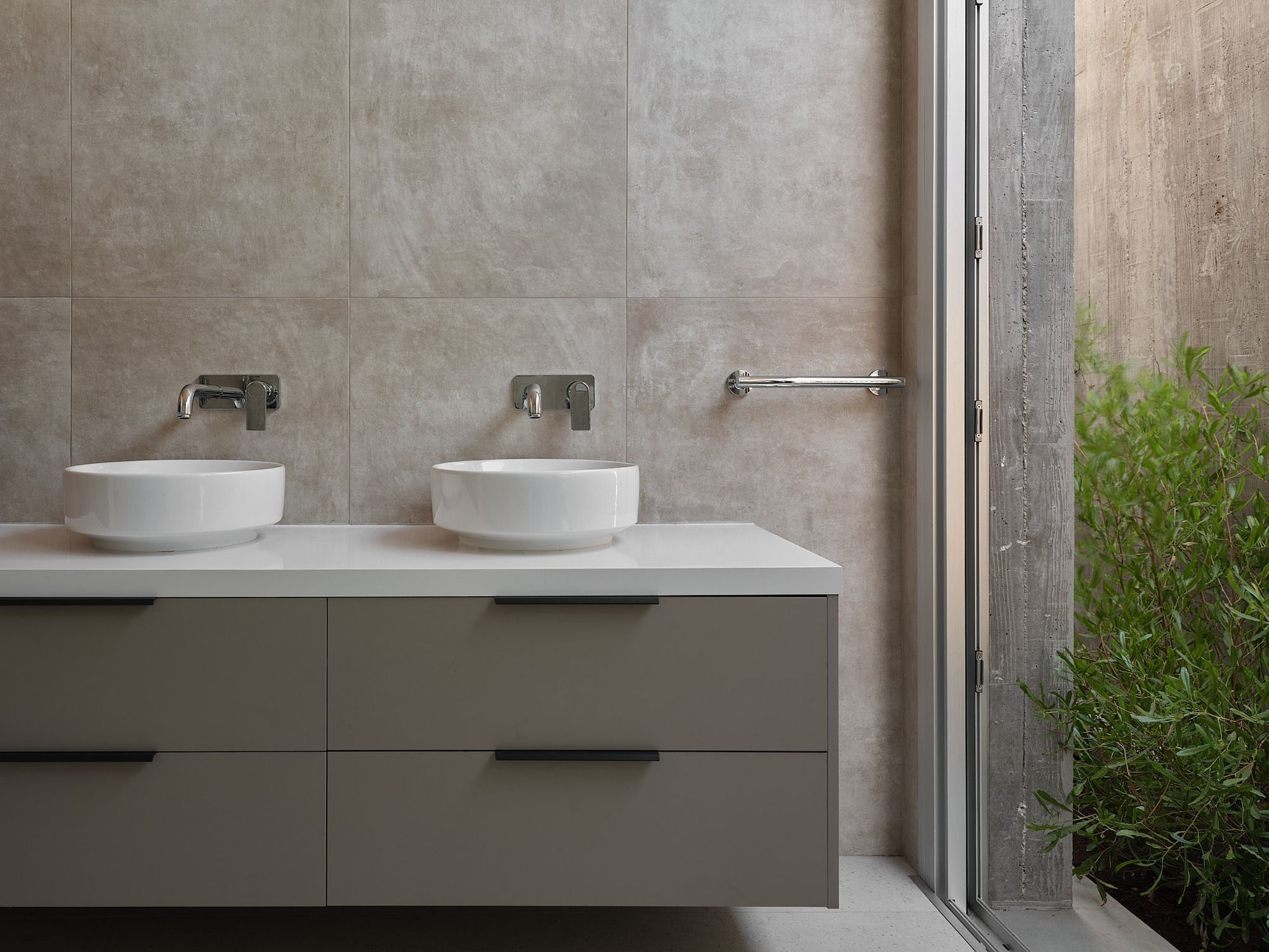 Double vessel sinks on a floating vanity beside a glazed door opening to a planted courtyard