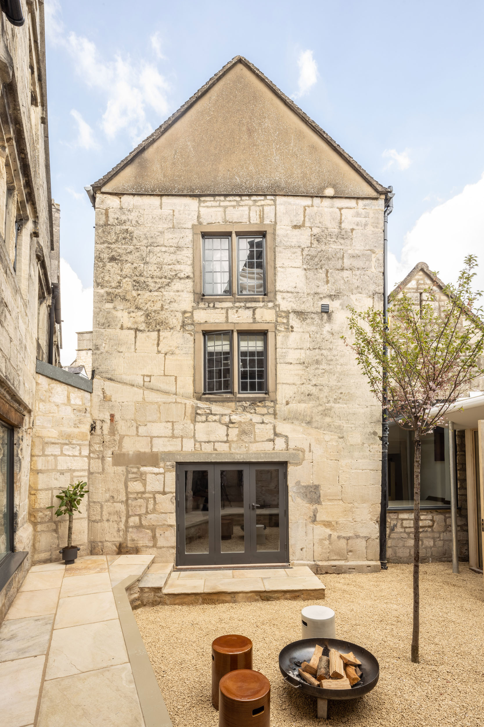 Courtyard view of the stone gable facade with new glazed doors and a small tree in gravel