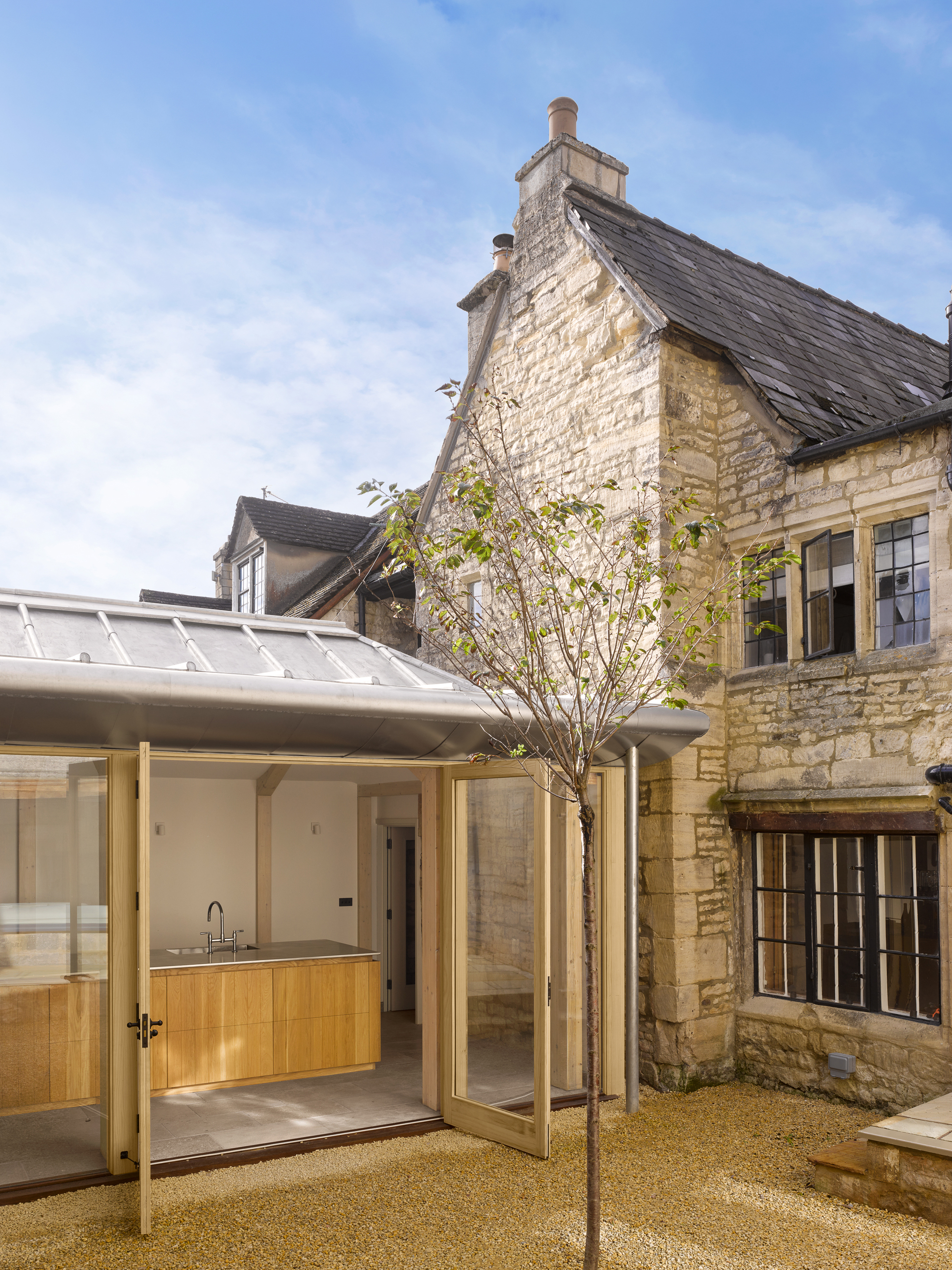 Courtyard showing the glazed extension with timber cabinetry opening onto gravel with a young tree